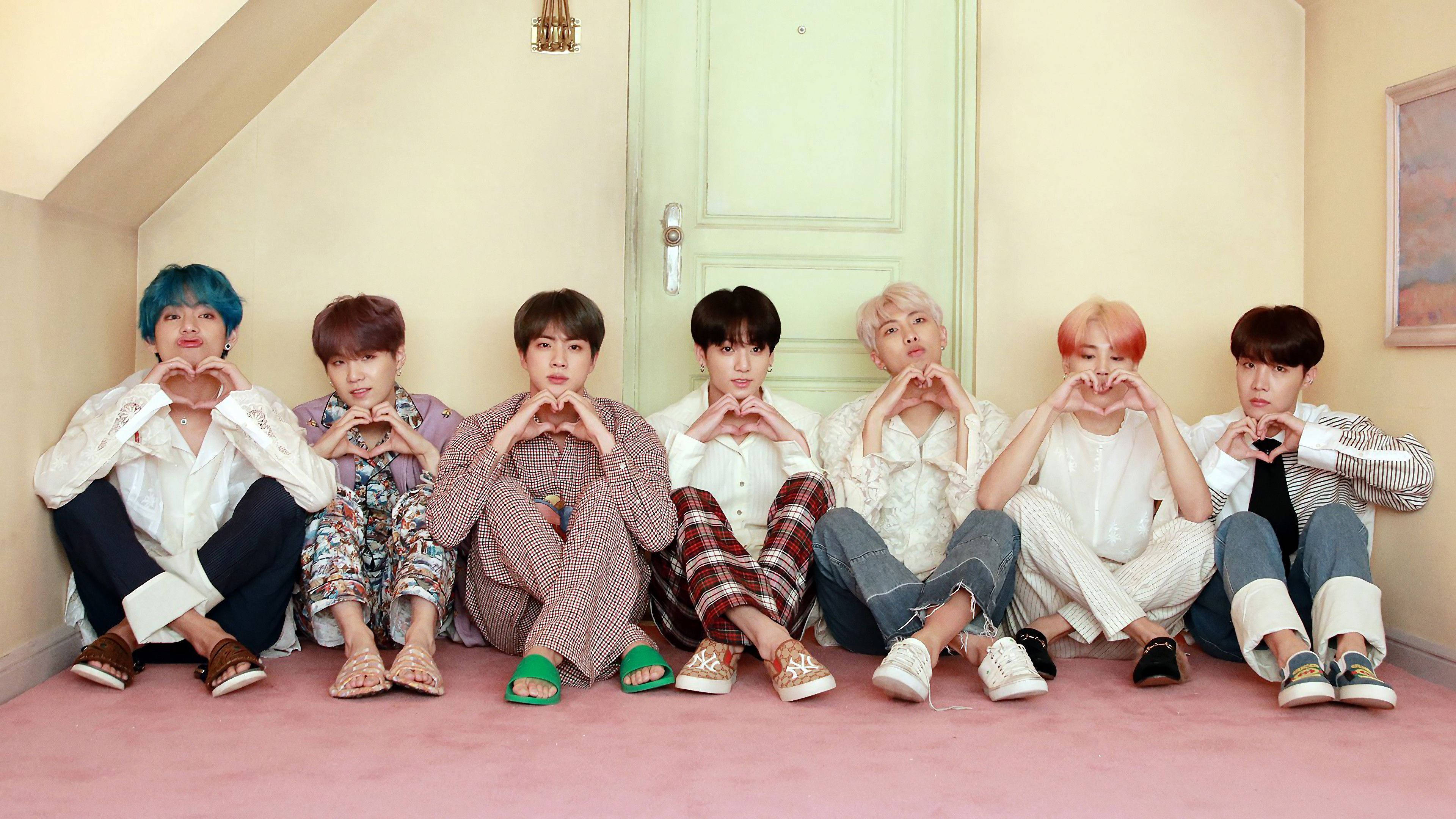 BTS 桌布 壁紙 — 七個擁有彩色頭髮的年輕男子坐在傾斜閣樓的粉紅色地板上，用手做出心形。