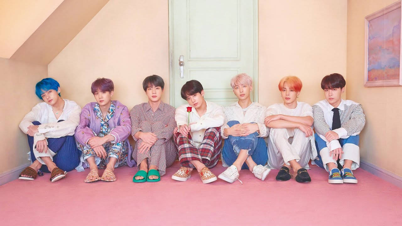 bts group cute 桌布 壁紙 — 七個擁有彩色頭髮的年輕男子隨意地坐在粉紅色地板上，身處一個柔和色調的閣樓房間。