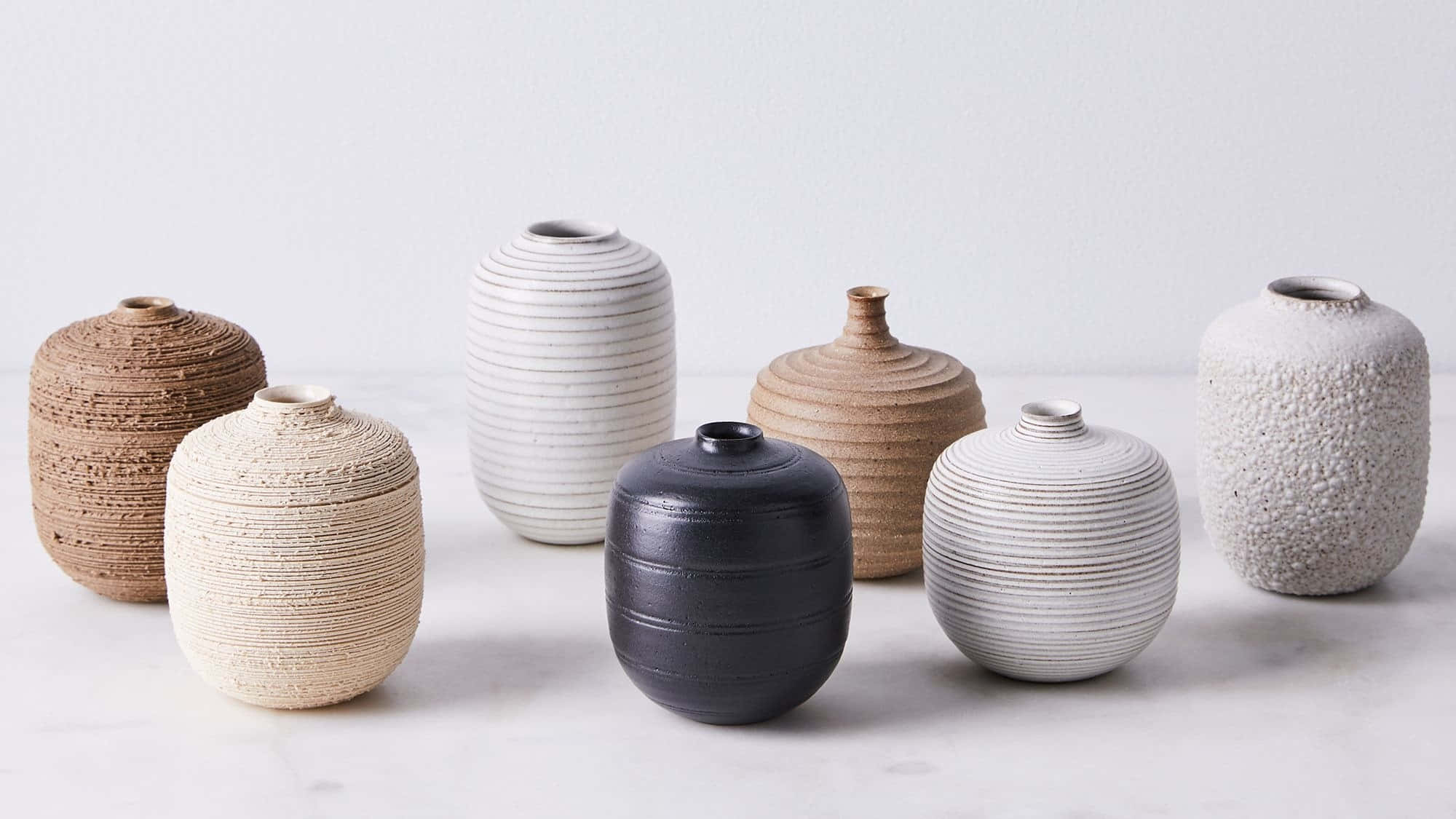 Ceramic 桌布 壁紙 — 七個極簡風格的陶瓷花瓶，表面帶有紋理，採用大地色調，排列在白色大理石表面上。