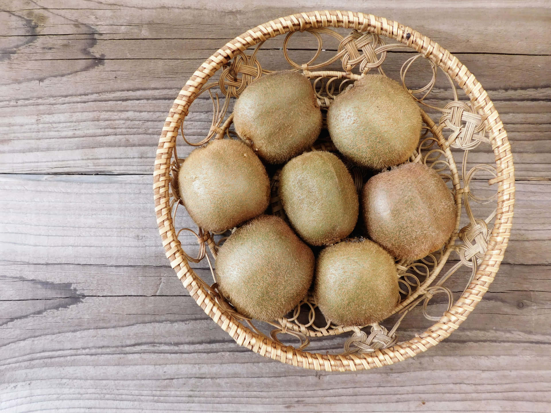 Kiwi 壁紙 — 七個毛茸茸的棕色奇異果放在一個編織柳條籃裡，擺在一個經風化的木質表面上。