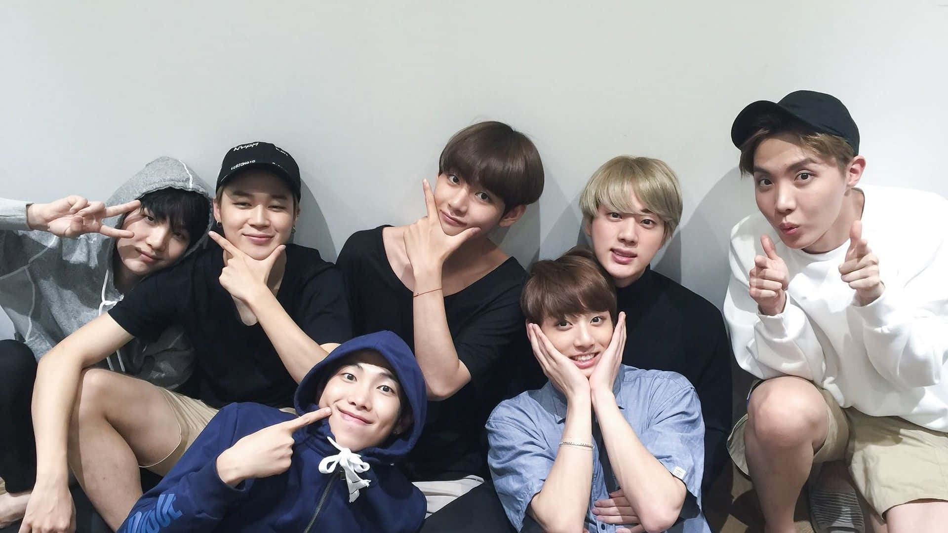 Bts Mac 桌布 壁紙 — 七個穿著休閒服的年輕男子在素牆前擺出趣怪的姿勢，做出和平手勢和鬼臉。