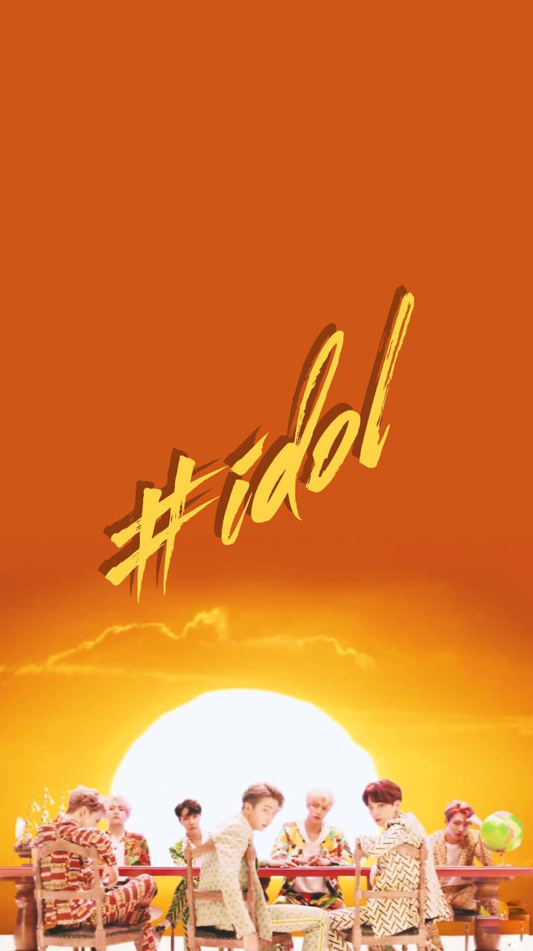The Idol 桌布 壁紙 — 七個穿著圖案服裝的男人坐在一張桌子前，背景是充滿活力的橙色日落，有一個大太陽和「#idol」文字。