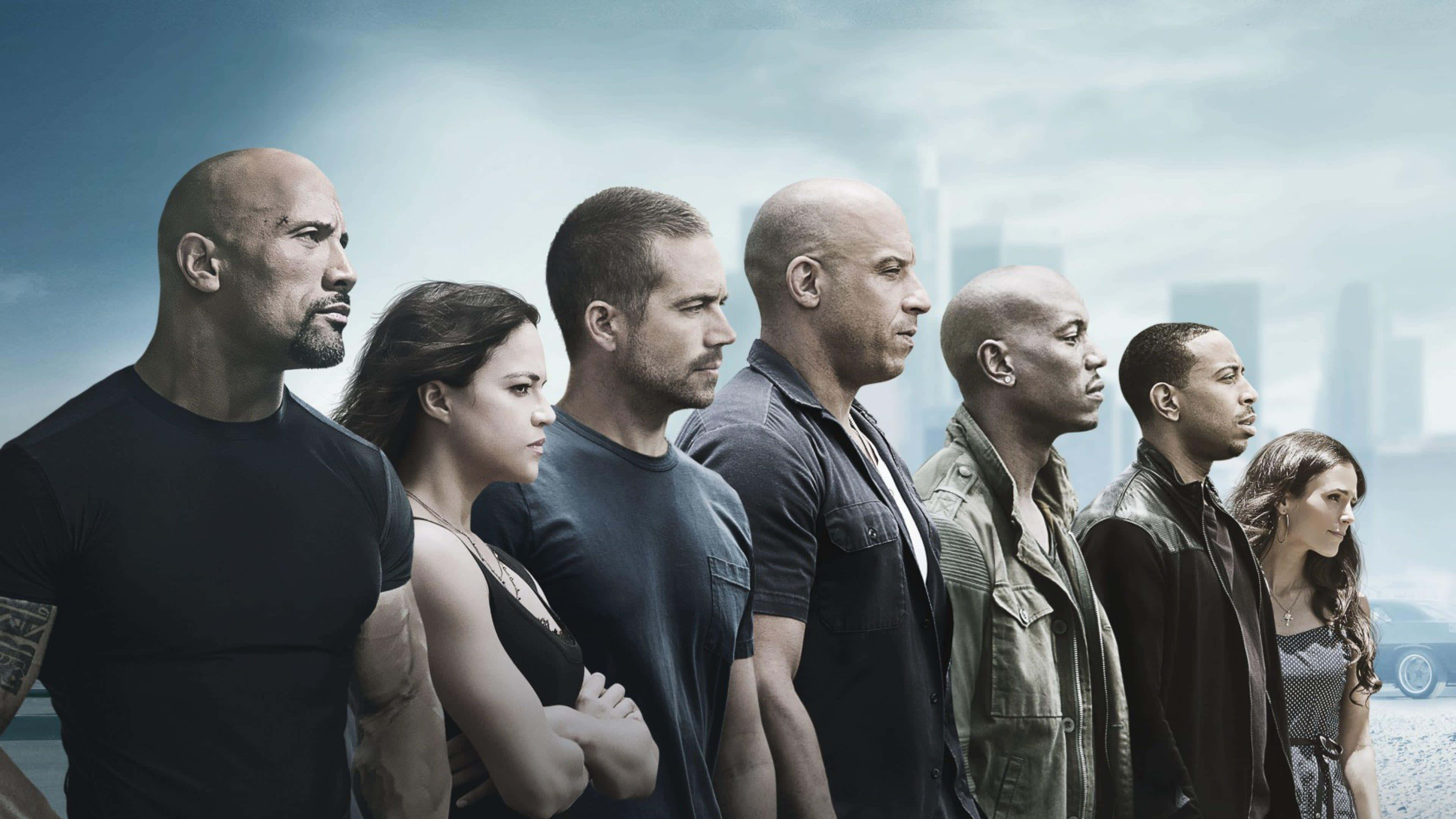 Fast And Furious 9 桌布 壁紙 — 七個穿著深色衣服的強烈電影角色在風暴天空下，堅定地站在模糊的城市天際線前。
