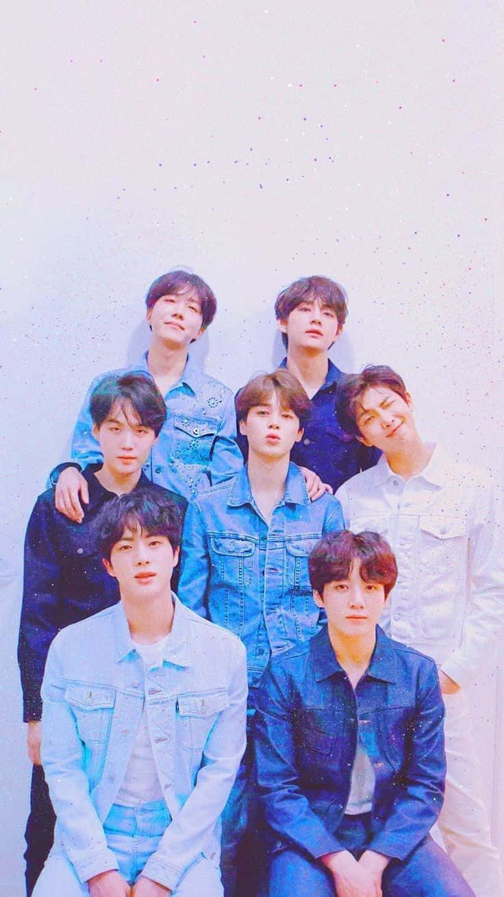 BTS 桌布 壁紙 — 七個穿著牛仔外套的年輕男子在柔和的粉彩背景前一起擺姿勢，背景帶有微妙的閃亮斑點。