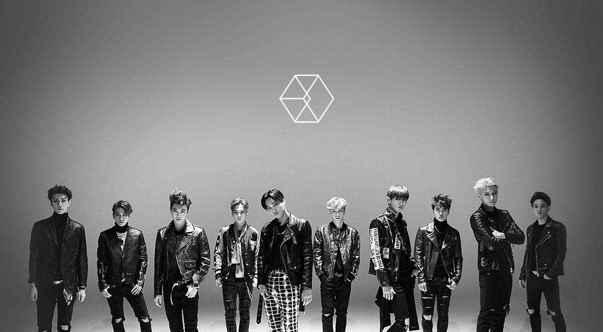 K-pop 桌布 壁紙 — 七個穿著皮夾克的男人自信地站在一個單色調的攝影棚中，上方有一個幾何標誌。