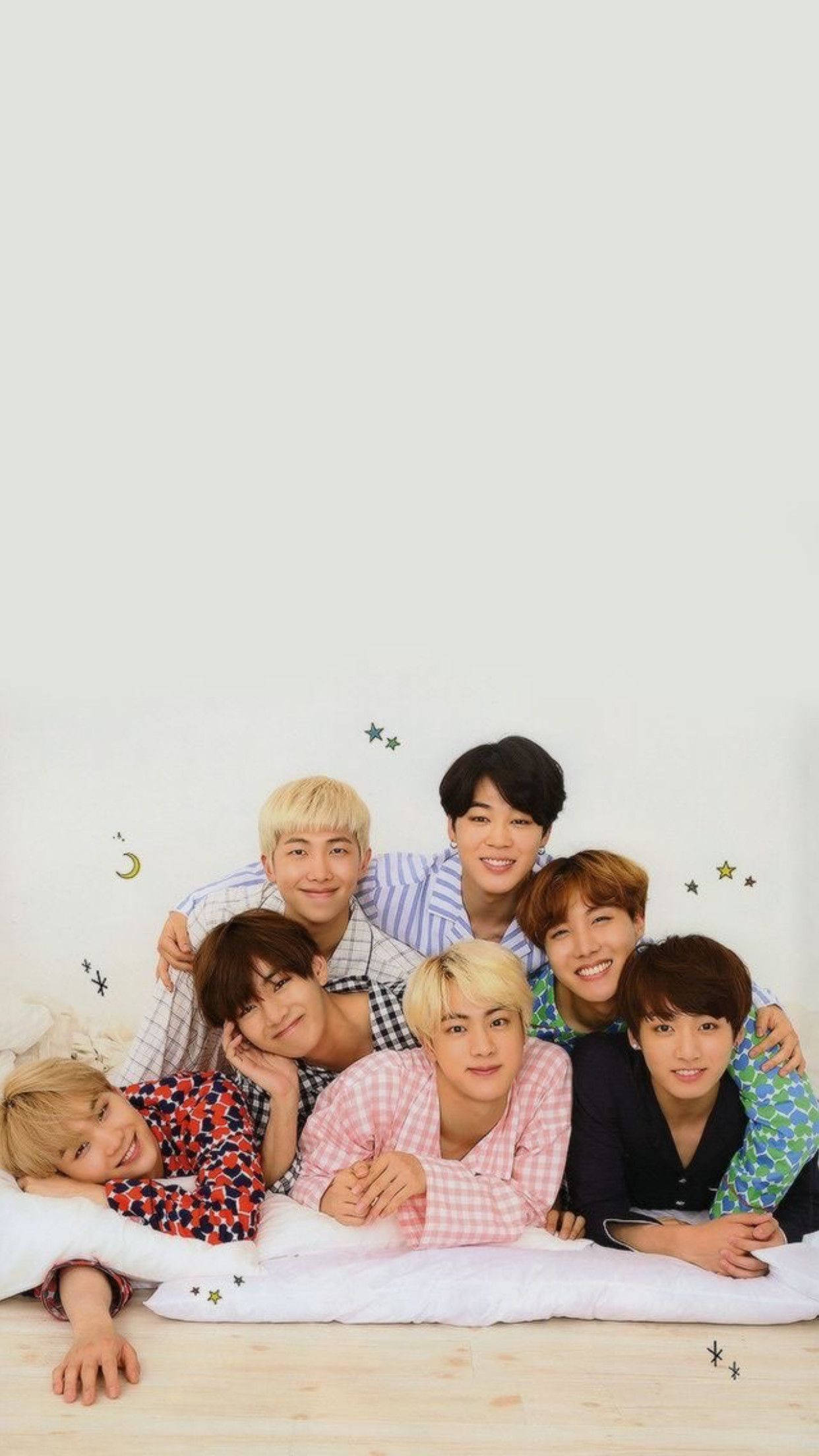 BTS 桌布 壁紙 — 七個穿著睡衣的年輕男子在床上一同微笑擺姿勢，背景是素面牆壁，上面有星星和月亮貼紙。