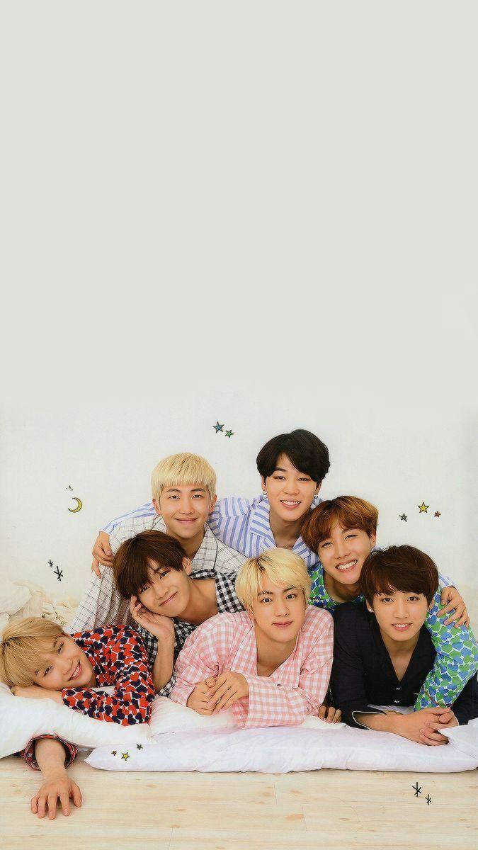 BTS 鎖定螢幕 桌布 壁紙 — 七個穿著睡衣的年輕男子在貼有星星和月亮貼紙的床上微笑擺姿勢，背景是素牆。