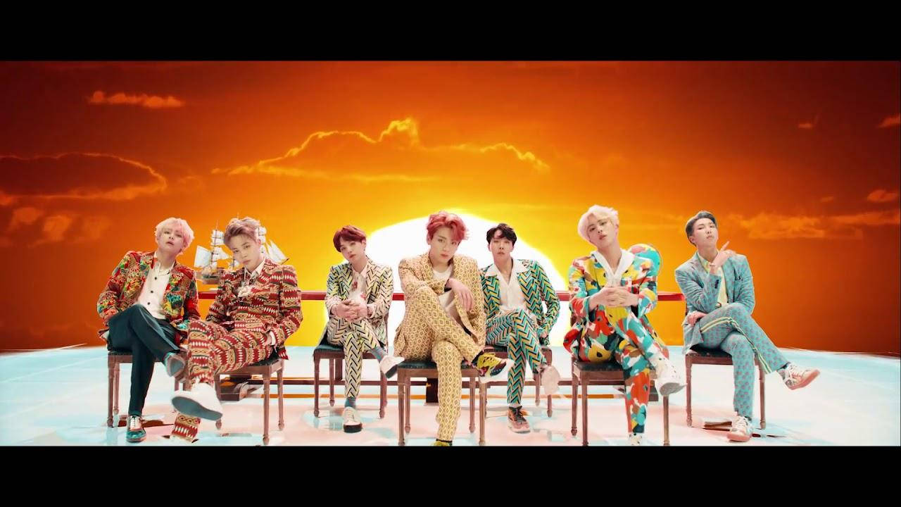 BTS 桌布 桌布 壁紙 — 七個穿著色彩繽紛圖案西裝的男人坐在椅子上，背景是火紅的橙色日落天空。