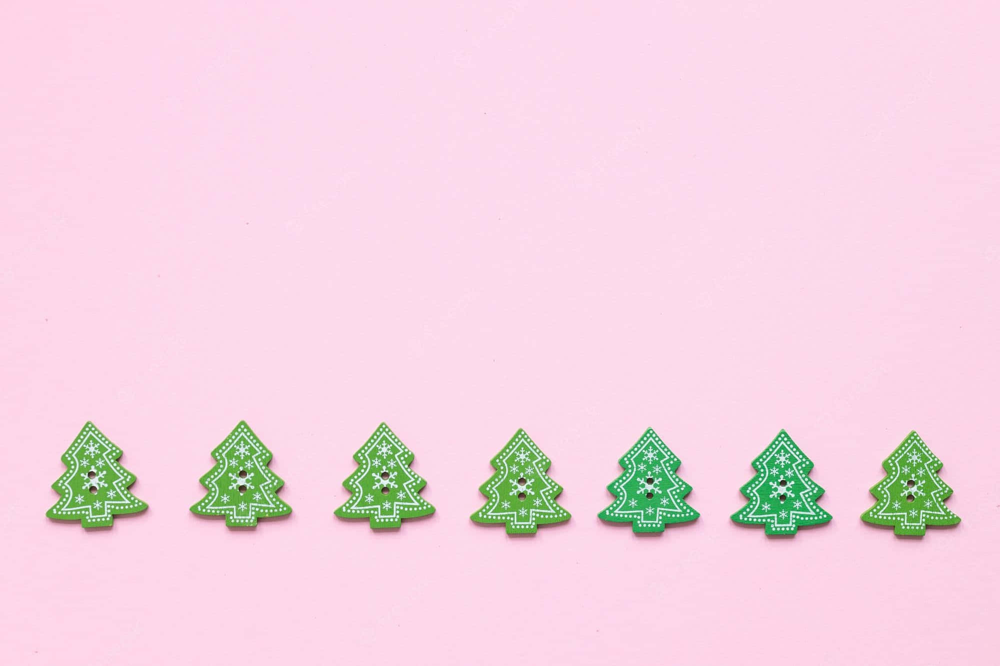 Pink Christmas Tree 桌布 壁紙 — 七個綠色聖誕樹形狀的鈕扣，帶有白色雪花圖案，排列在柔和的粉紅色背景上。