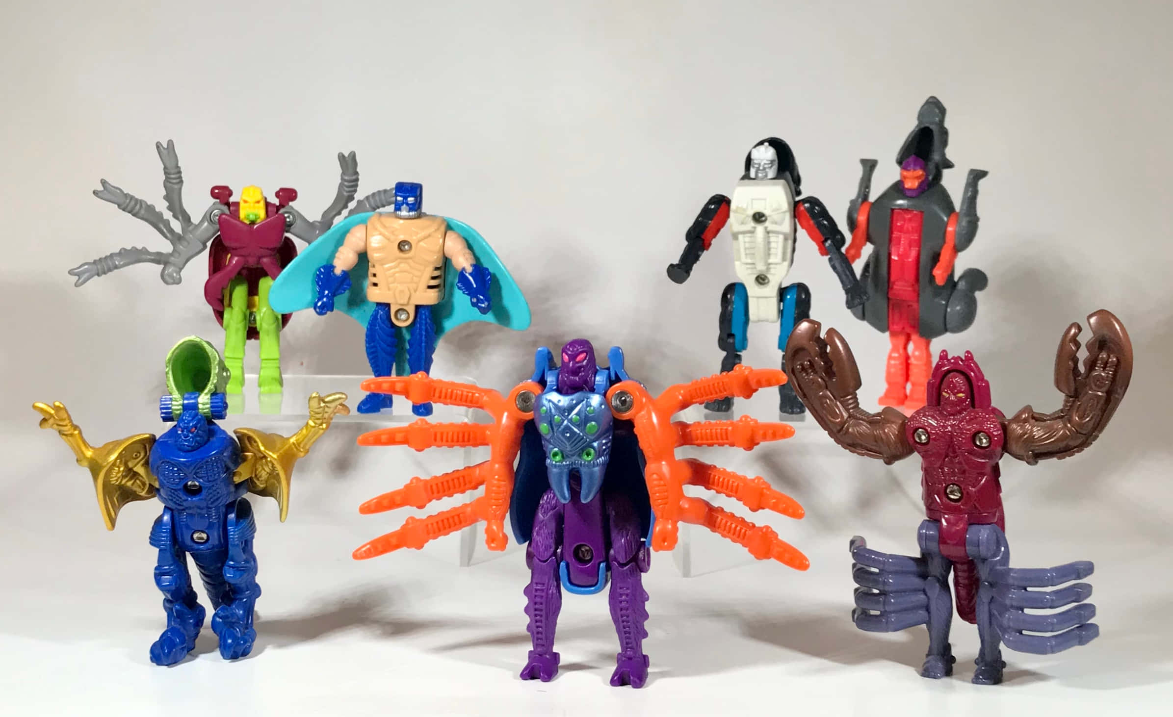 toys 桌布 壁紙 — 七個色彩繽紛的塑膠動作人偶，帶有昆蟲型和機器人設計，在純白色背景前擺出姿勢。