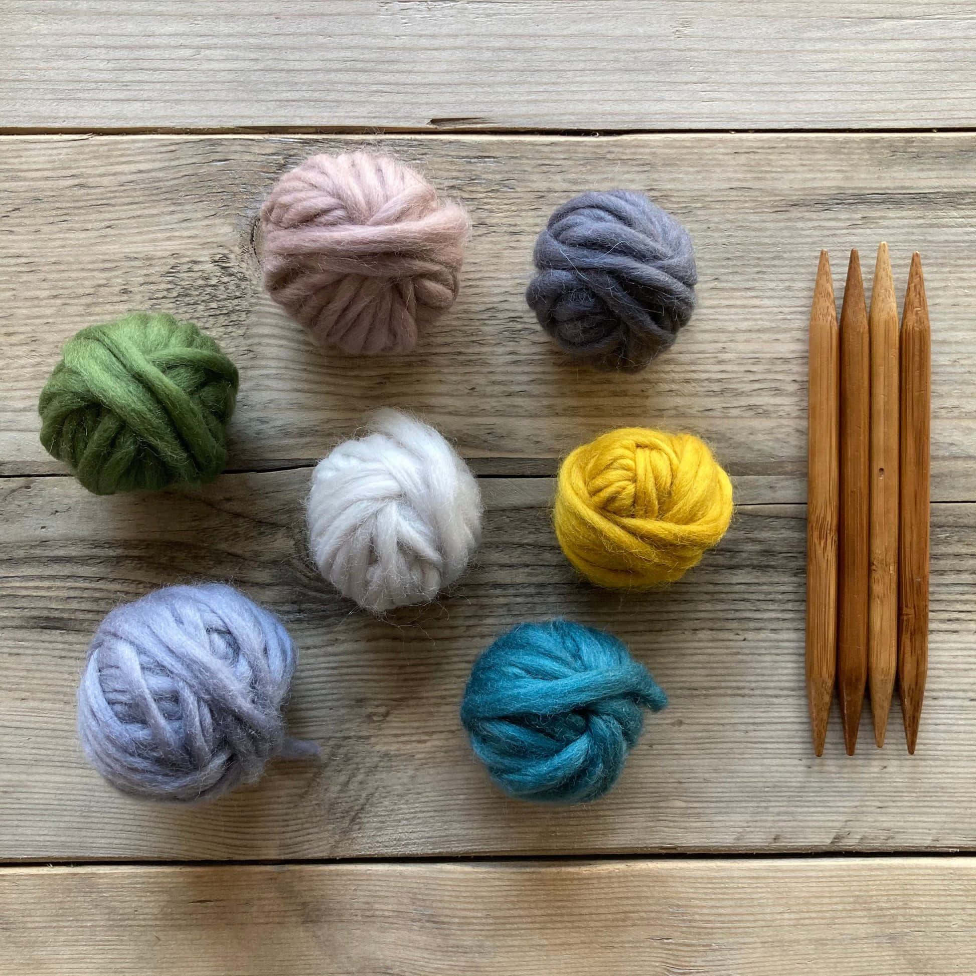 clothing 桌布 壁紙 — 七個色彩繽紛的毛線球和四根木製編織針整齊地排列在風化的木質表面上。