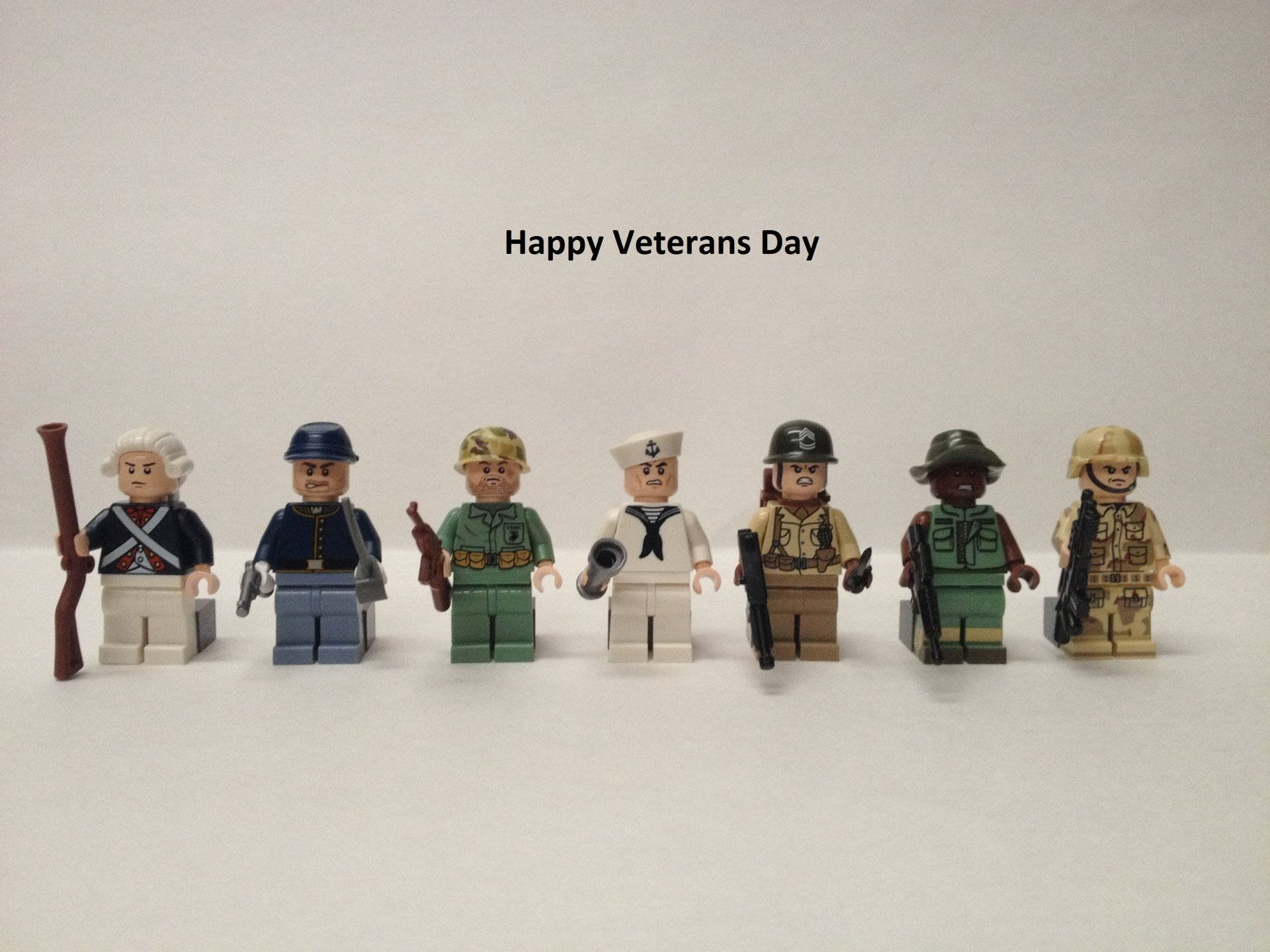 Veterans 桌布 壁紙 — 七個身穿不同軍服的LEGO士兵人偶排成一排，背景為純白色，上方有「Happy Veterans Day」字樣。