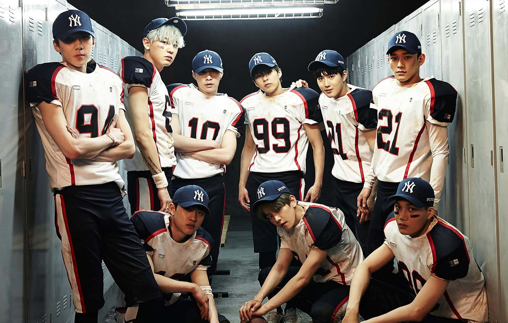 EXO 桌布 壁紙 — 七個身穿棒球服的年輕男子在光線昏暗的更衣室裡自信地擺姿勢，旁邊有金屬置物櫃。