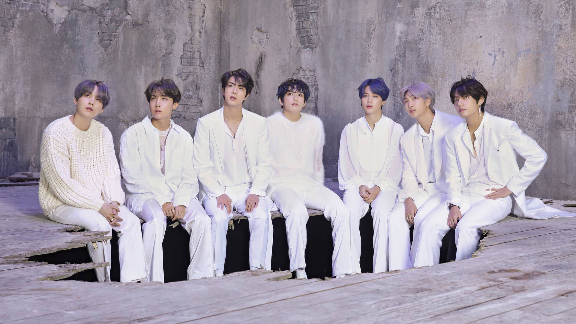 BTS 2021 桌布 壁紙 — 七個身穿白色服裝的男人坐在木製平台上，背景是風化的混凝土牆，帶有微妙的紫色頭髮點綴。