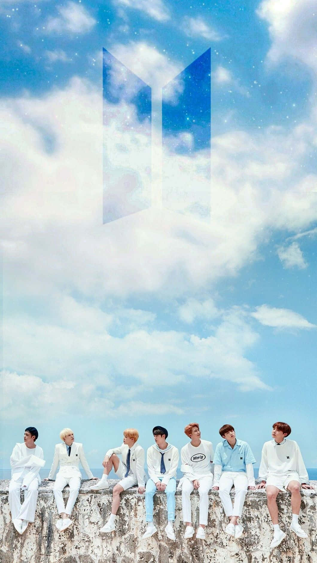 BTS 桌布 壁紙 — 七個身穿白色服裝的男人坐在石頭邊緣上，天空湛藍，有蓬鬆的雲朵，上方漂浮著發光的BTS標誌。