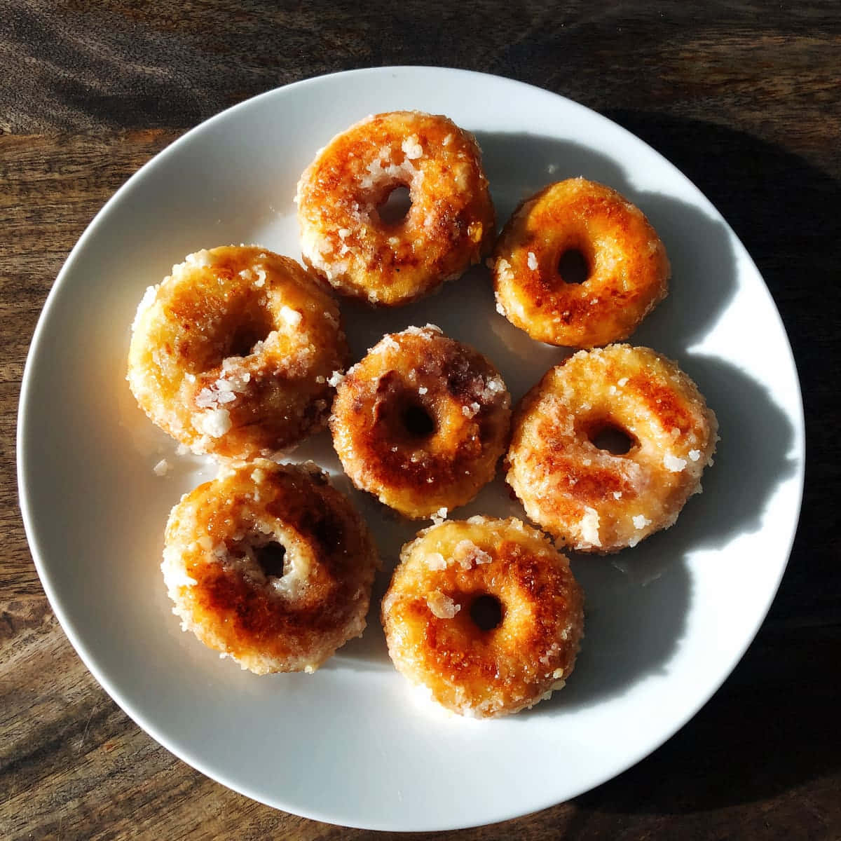 Glazed Donut 桌布 壁紙 — 七個金黃色糖霜甜甜圈放在深色木桌上的白色盤子上。
