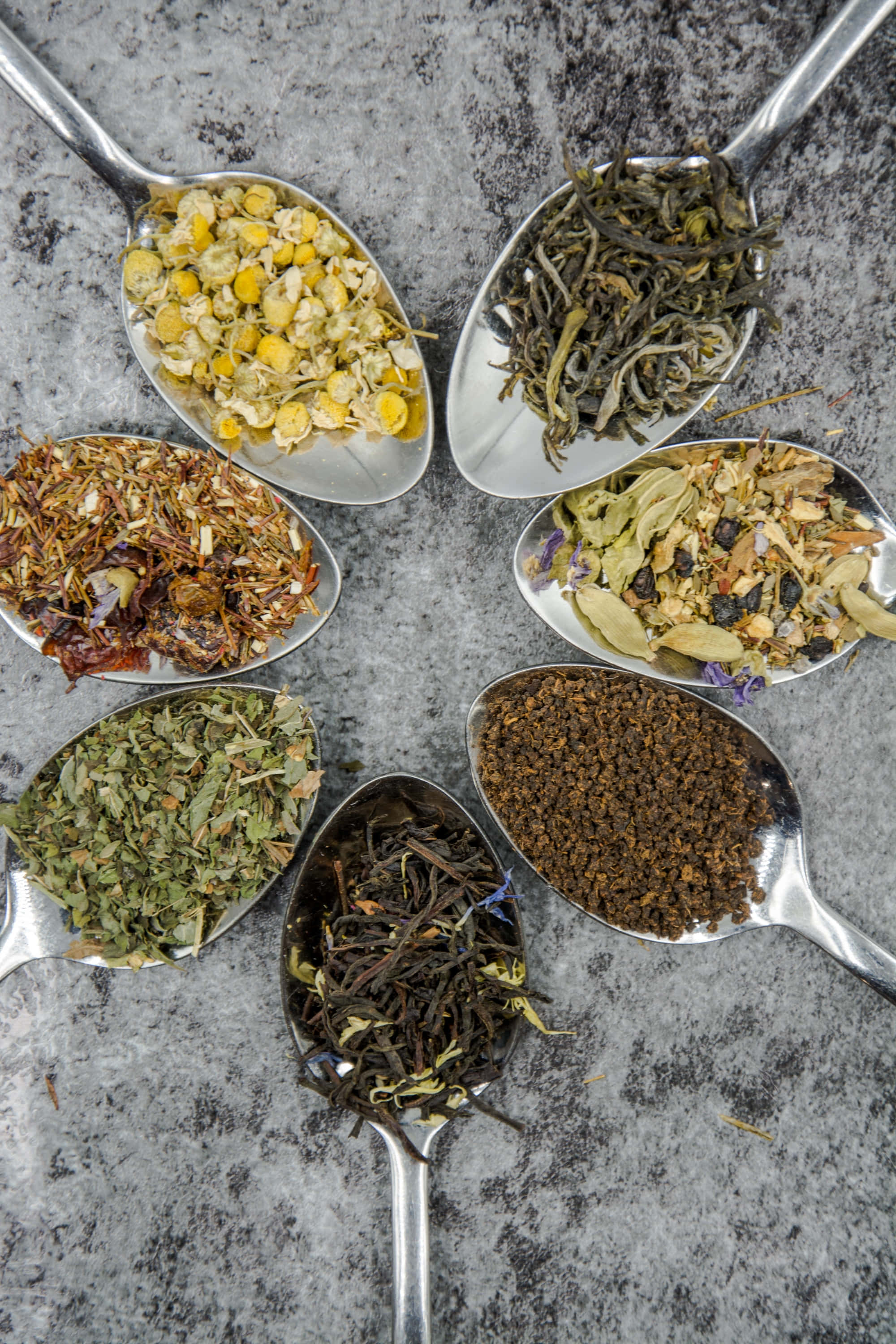Spices 桌布 壁紙 — 七個銀匙盛載著多種乾茶和香草，在灰色石面上排列成圓形。