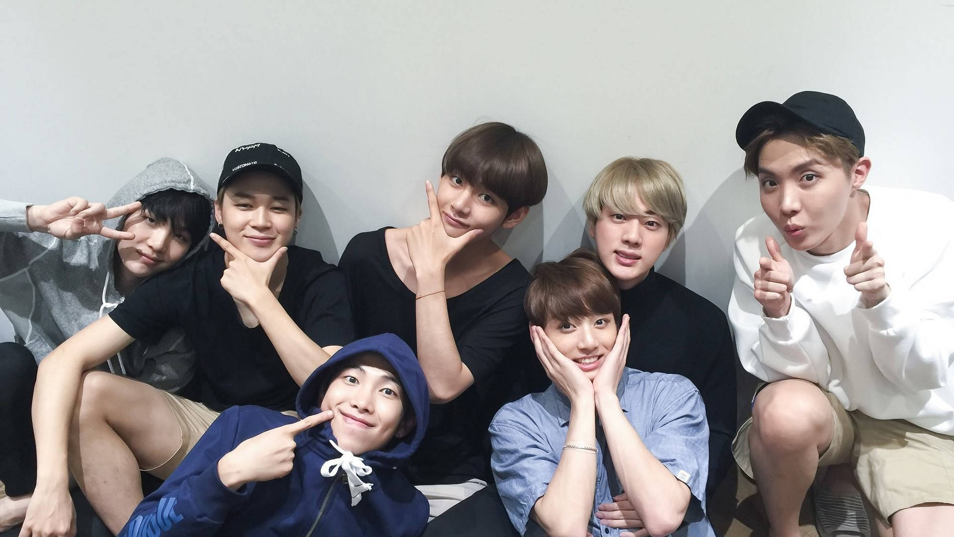BTS 桌布 壁紙 — 七名年輕男子穿著休閒服裝，在素牆前擺出俏皮姿勢，做出和平手勢和鬼臉。