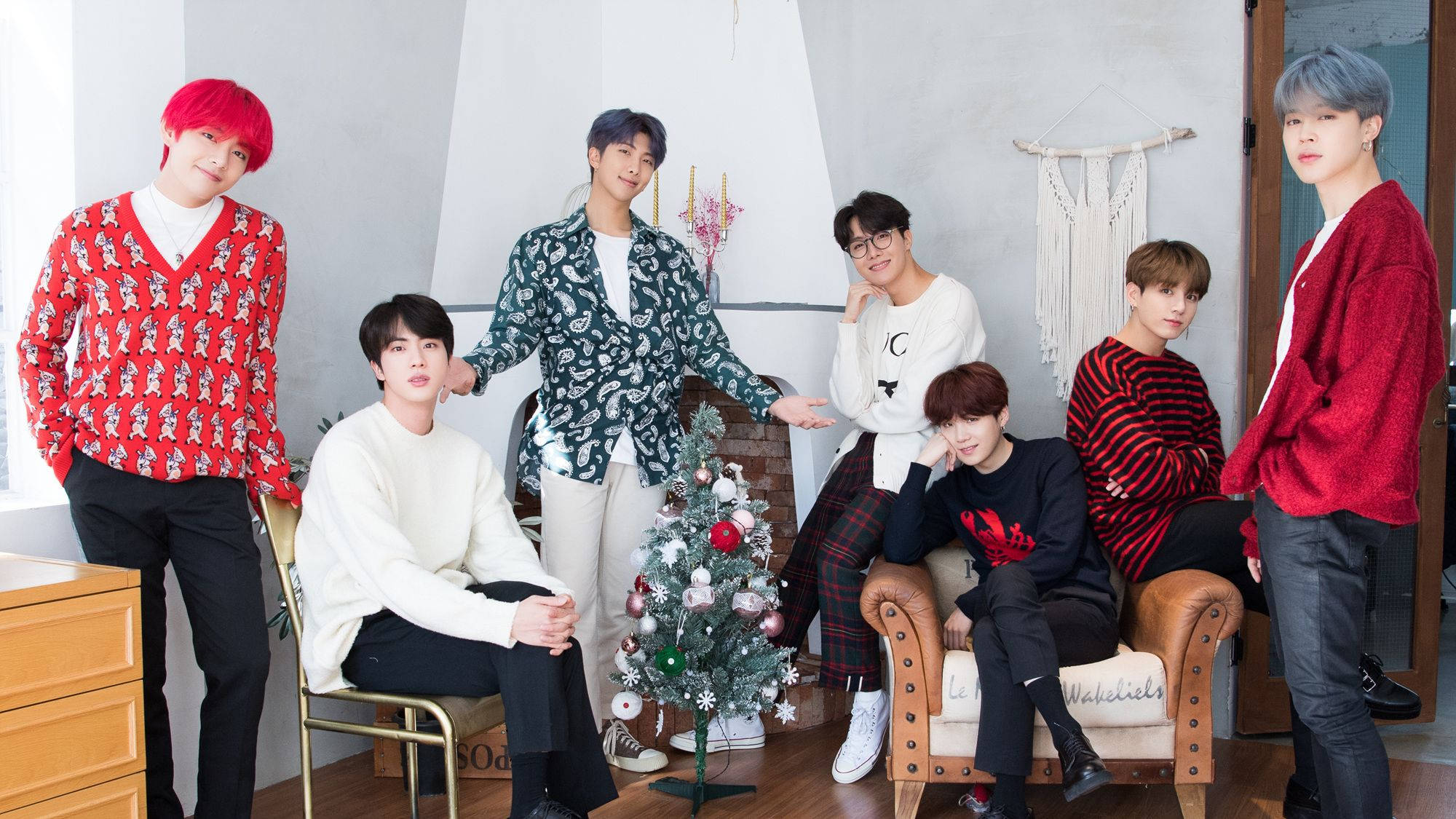 BTS 桌布 桌布 壁紙 — 七名年輕男子穿著節日毛衣，在裝飾好的聖誕樹周圍擺姿勢，室內環境舒適。