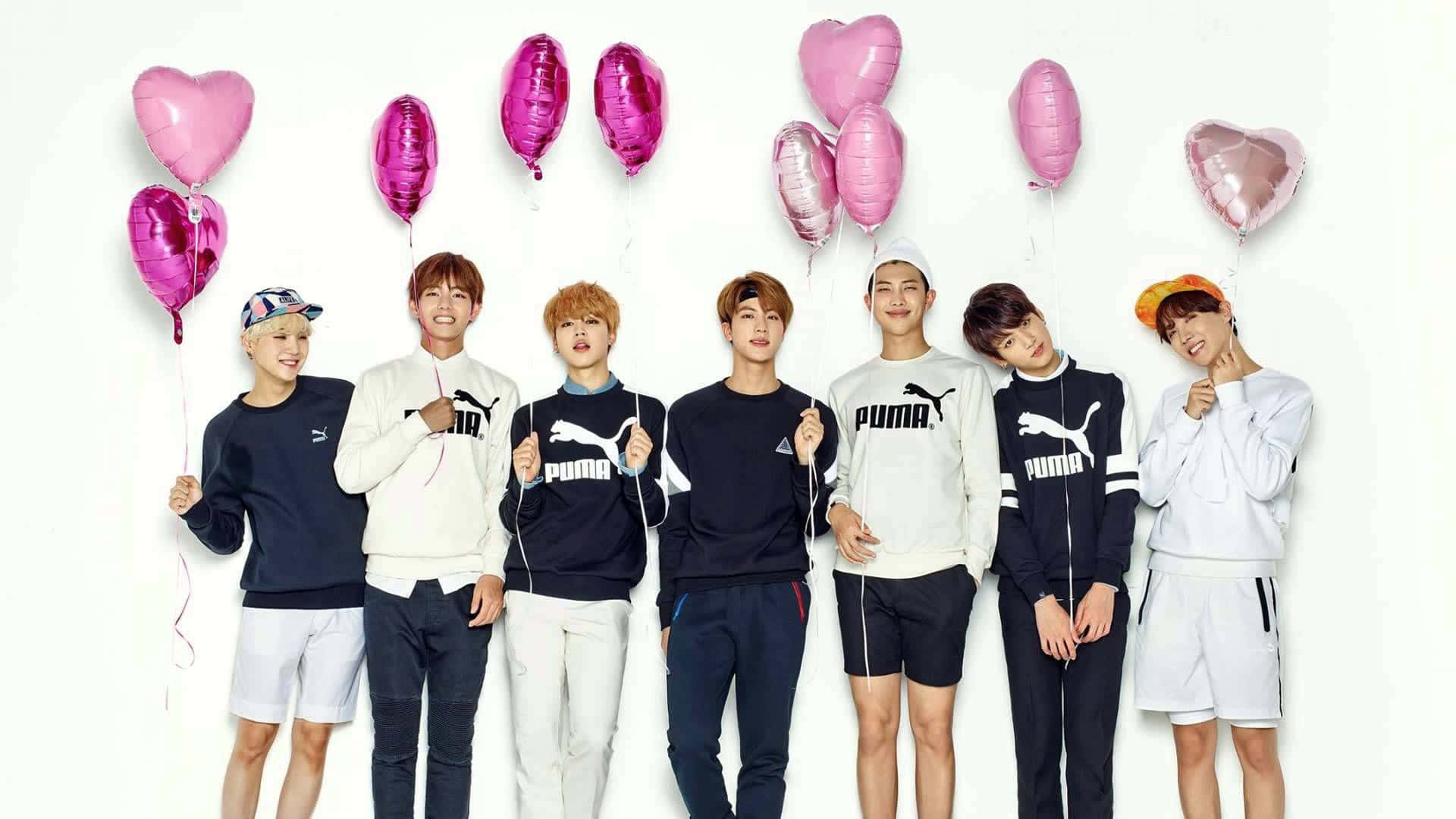 Bangtan Sonyeondan 桌布 壁紙 — 七名身穿Puma運動服的年輕男性在白色背景前愉快地擺姿勢，背景有粉紅色心形和橢圓形氣球。