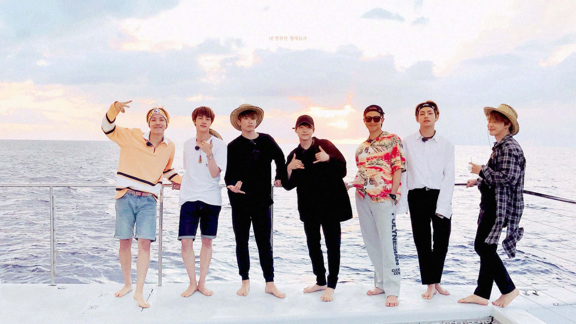 Bts Mac 桌布 壁紙 — 七名身穿休閒夏季服裝的男子赤腳在船甲板上擺姿勢，背景是柔和的日落天空和寧靜的海洋。