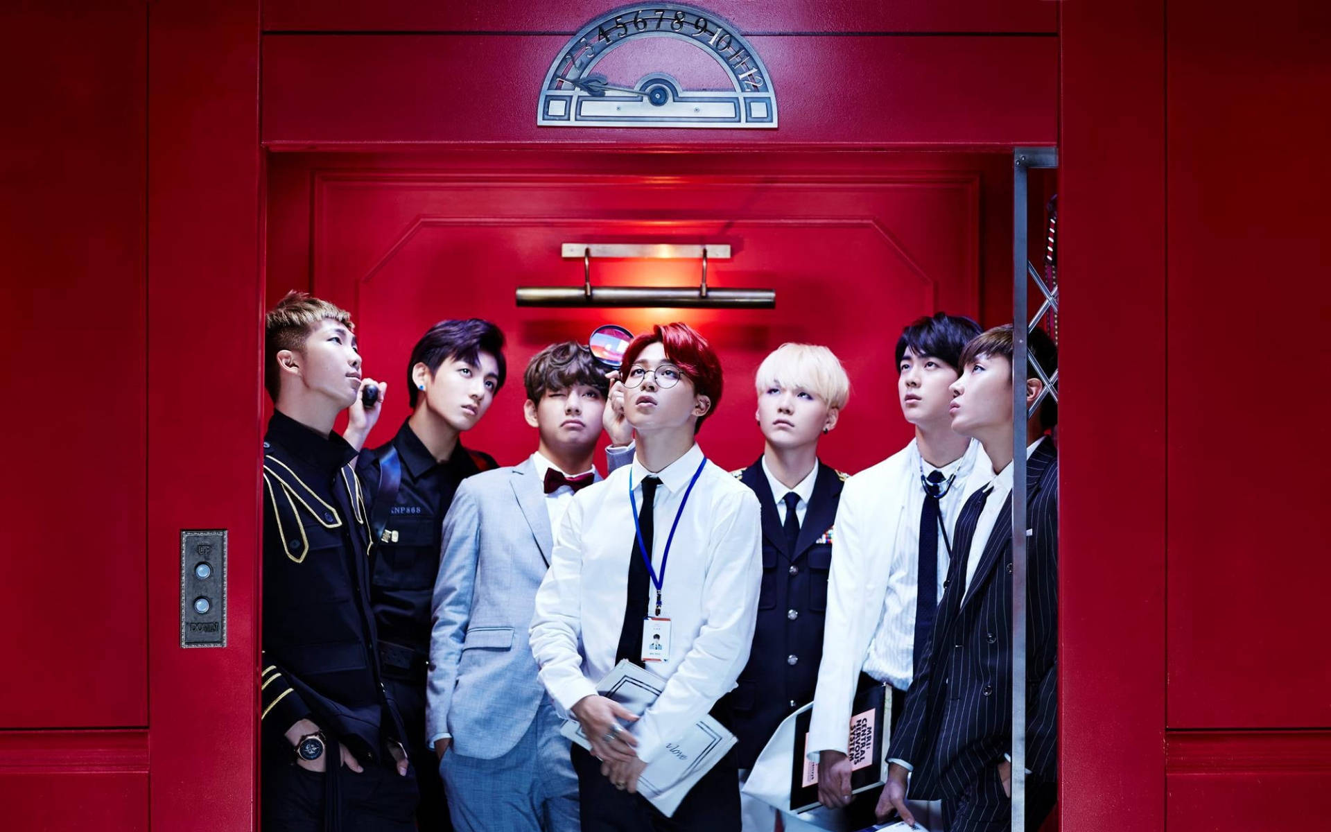 BTS 桌布 壁紙 — 七名身穿正式西裝的男子站在一個搶眼的紅色電梯內，抬頭仰望，表情充滿好奇與興趣。