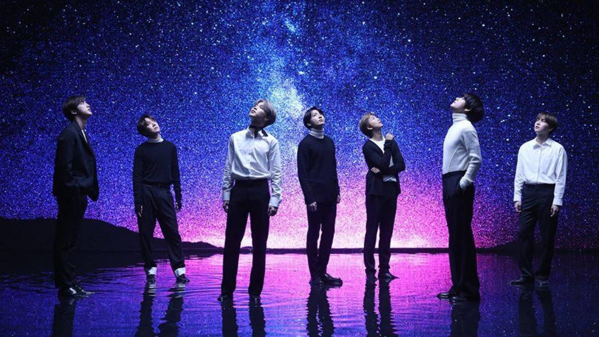 BTS 桌布 桌布 壁紙 — 七名身穿正裝的男子站在反光舞台上，仰望充滿活力的宇宙星空背景。