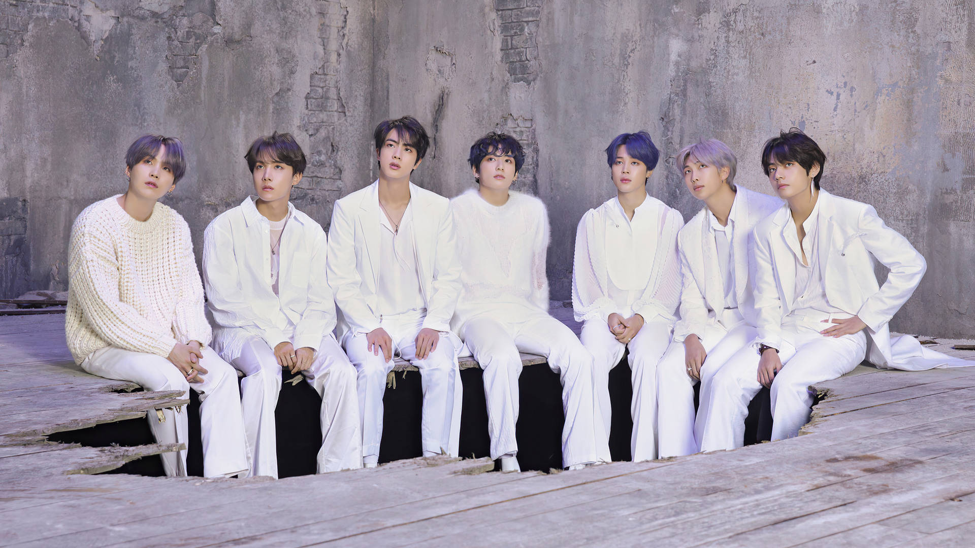 BTS 桌布 壁紙 — 七名身穿白色服裝的男子坐在木製平台上，背景是風化的混凝土牆，帶有冷色調燈光。
