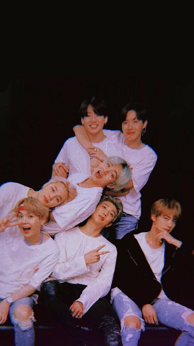 bts iPhone 桌布 壁紙 — 七名身穿白襯衫和破洞牛仔褲的年輕男子在黑色背景前擺出俏皮姿勢，帶有閃亮效果。