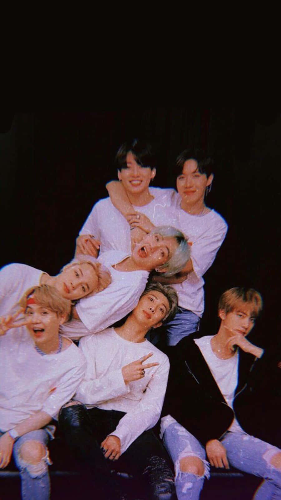 BTS 桌布 壁紙 — 七名身穿白襯衫和破洞牛仔褲的年輕男性在黑色背景前以鮮豔燈光嬉戲擺姿勢。