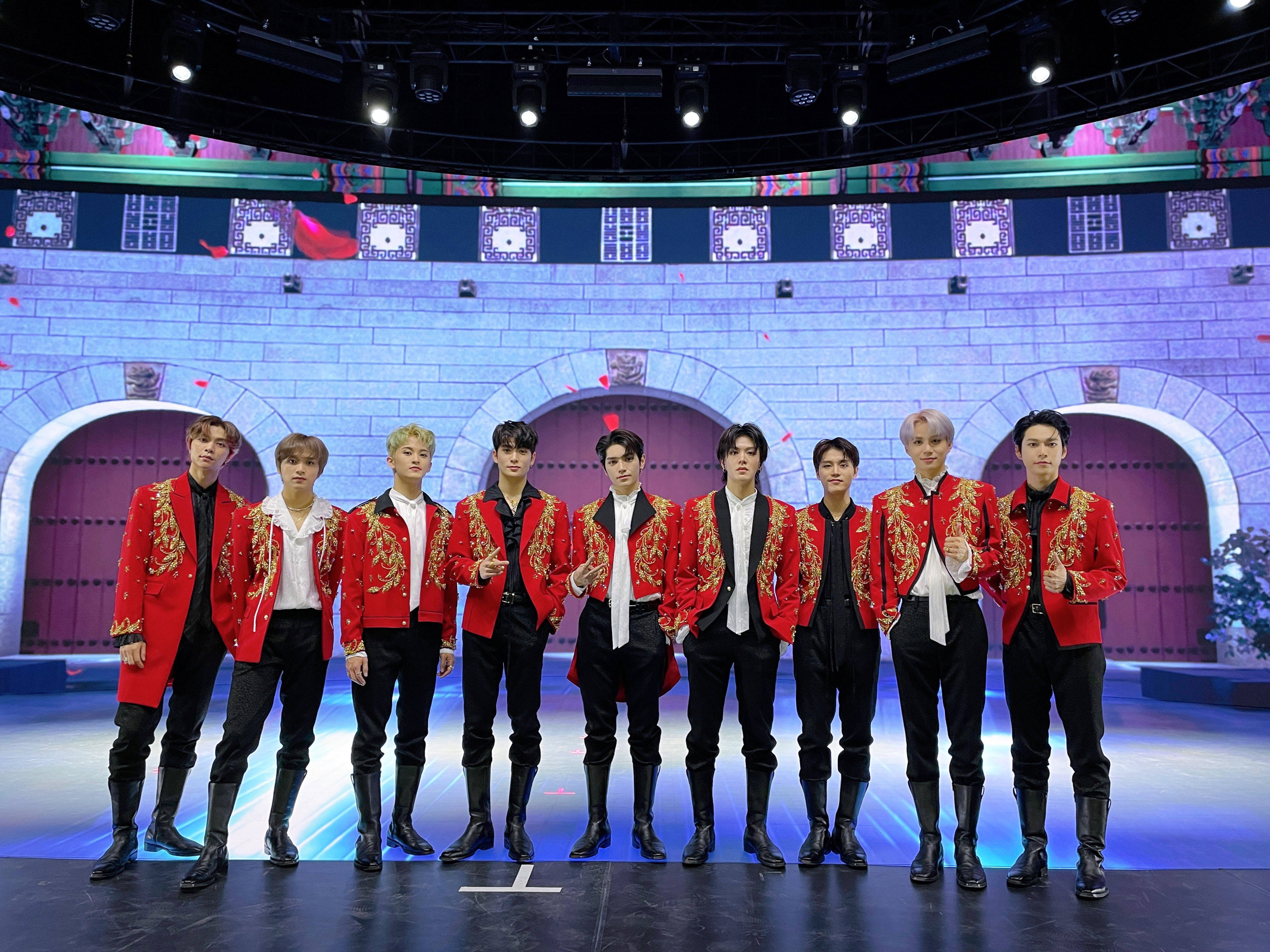Nct 桌布 壁紙 — 七名身穿華麗紅色外套的男子在城堡主題背景和發光藍色地板的舞台上自信地擺姿勢。