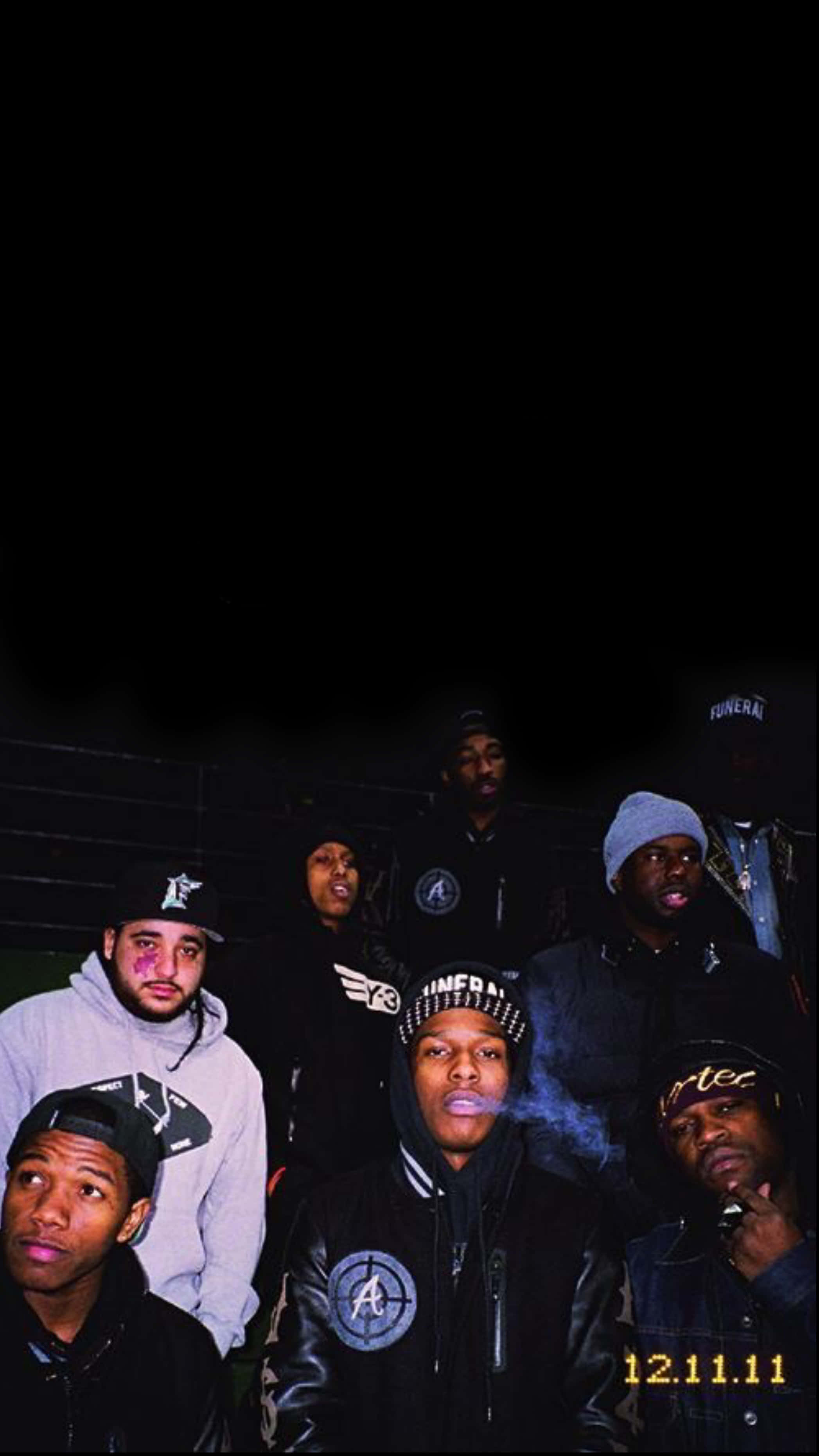 Rappers 桌布 壁紙 — 七名身穿連帽衫和帽子的男性在夜晚的暗牆前擺姿勢，一人吐煙，另一人拿著麥克風。