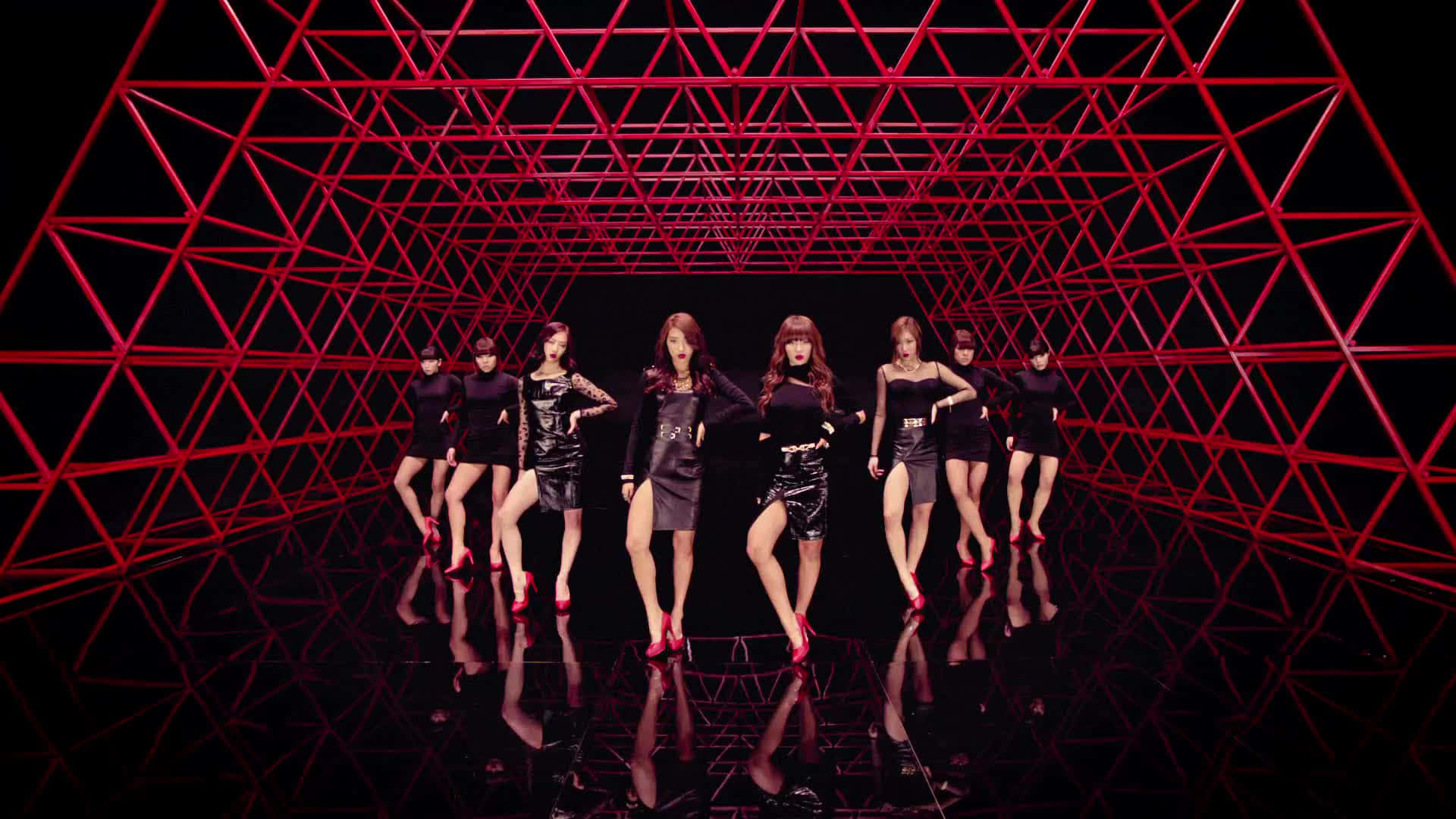 K-pop 桌布 壁紙 — 七名身穿黑色服裝和紅色高跟鞋的女性，在發光的紅色幾何隧道和反射地板下擺出同步姿勢。