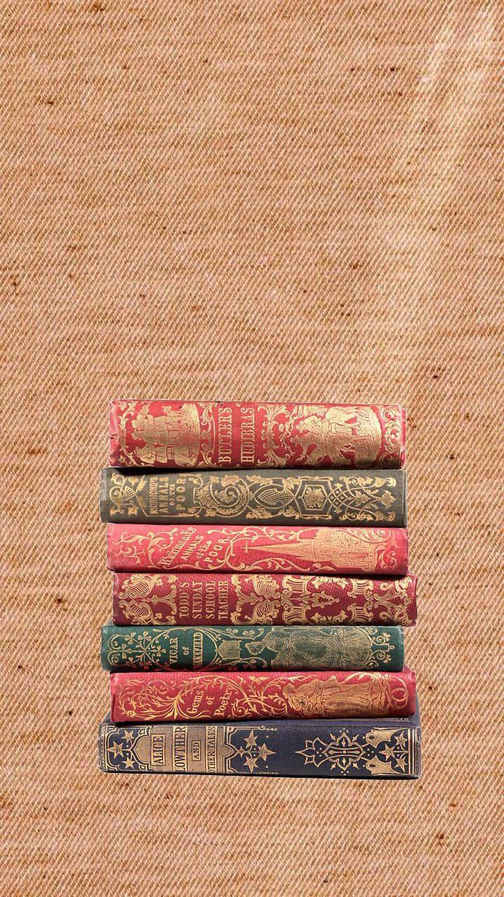 Books iPhone 桌布 壁紙 — 七本裝飾華麗的復古書籍，帶有金色浮雕書脊，垂直放置在帶有紋理的米色織物背景上。