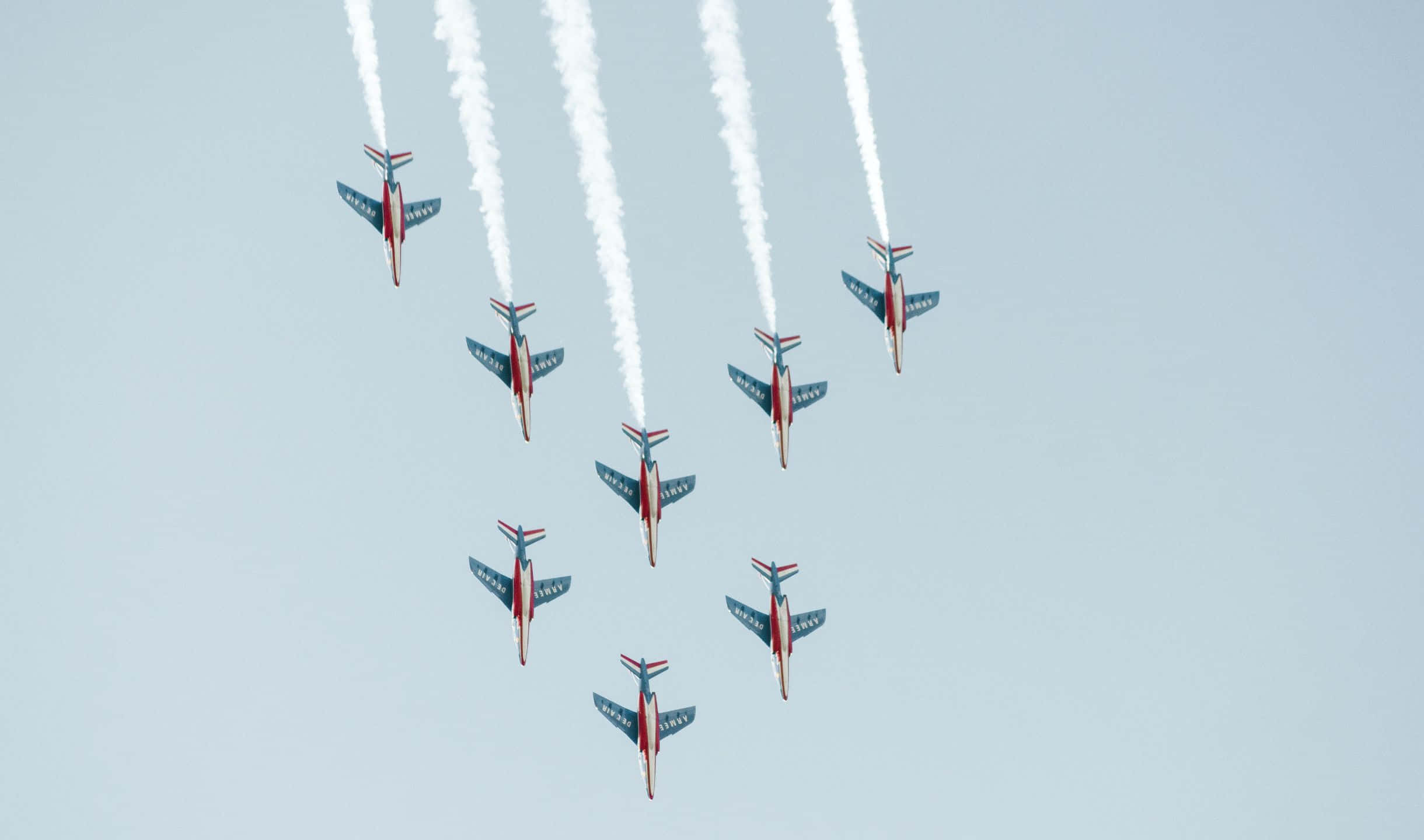 2440x1440 Small Planes 桌布 壁紙 — 七架紅、白、藍色噴射機以緊密編隊飛行，在淡藍色天空中留下濃厚的白色煙霧軌跡。
