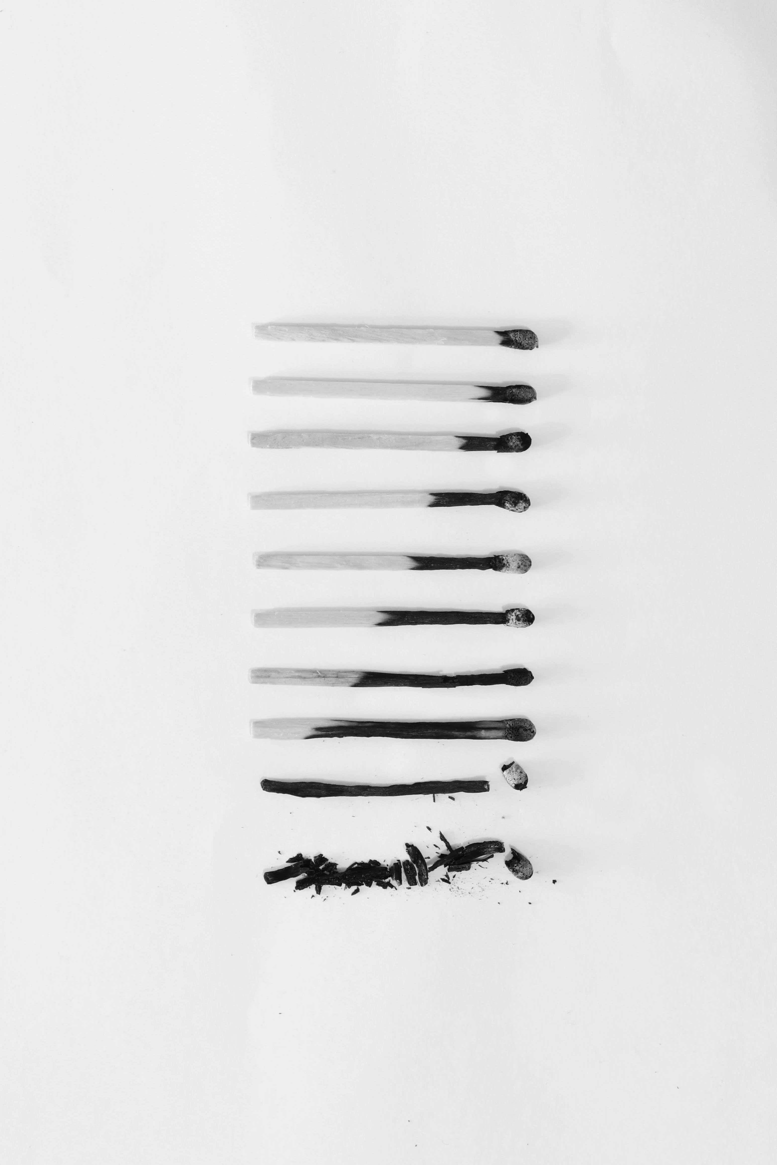 Aesthetic Black And White 桌布 壁紙 — 七根燒過的火柴垂直排列在白色背景上，下方散落著灰燼。