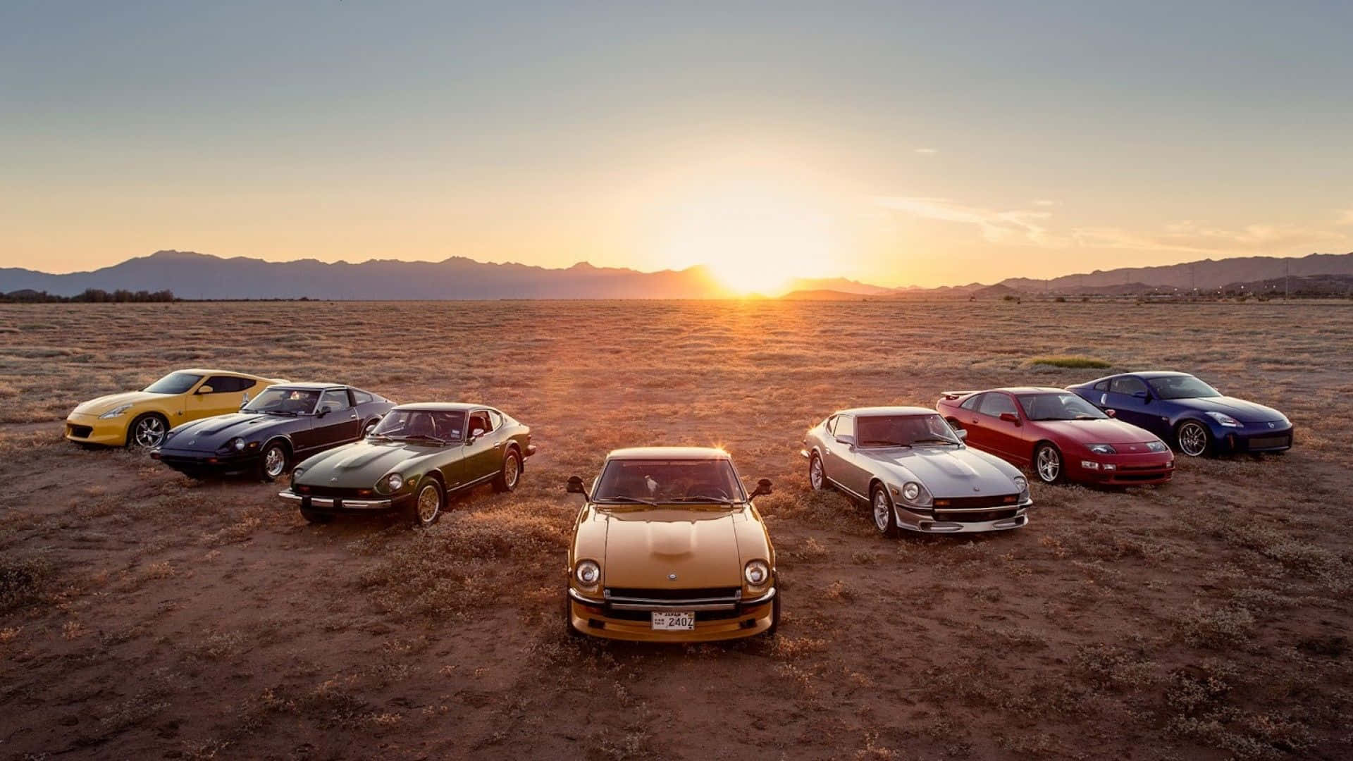 Datsun 桌布 壁紙 — 七輛經典跑車在夕陽下閃耀，橫跨廣闊的沙漠平原，遠山依稀可見。