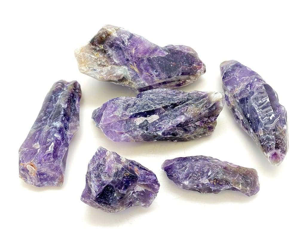 紫水晶 桌布 壁紙 — 七顆帶有深紫色和白色紋理的天然紫水晶原石，放置在明亮的白色表面上。