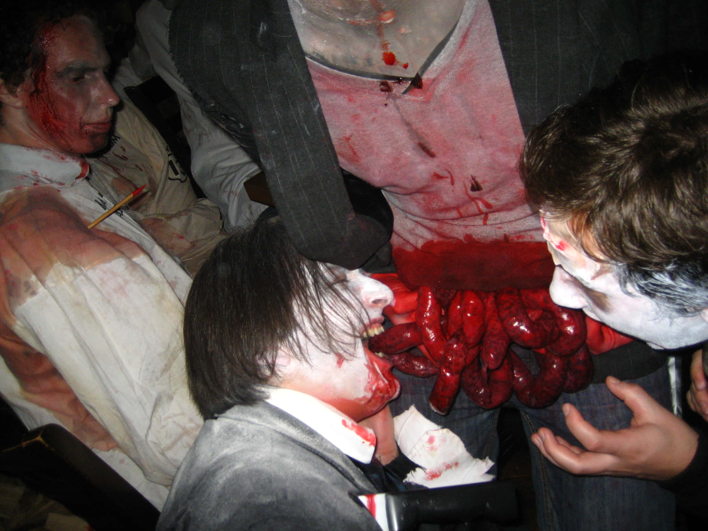 Real Zombie 桌布 壁紙 — 三人在黑暗房間中穿著恐怖萬聖節服裝，帶有假血和暴露的腸道。