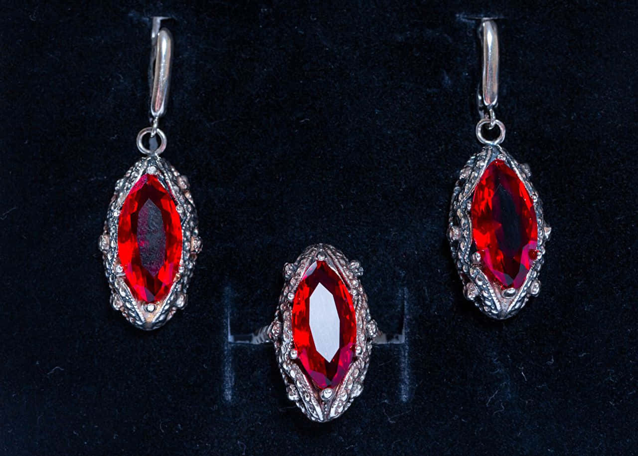 Earrings 桌布 壁紙 — 三件銀飾鑲有馬眼形紅寶石，展示在深色天鵝絨上。