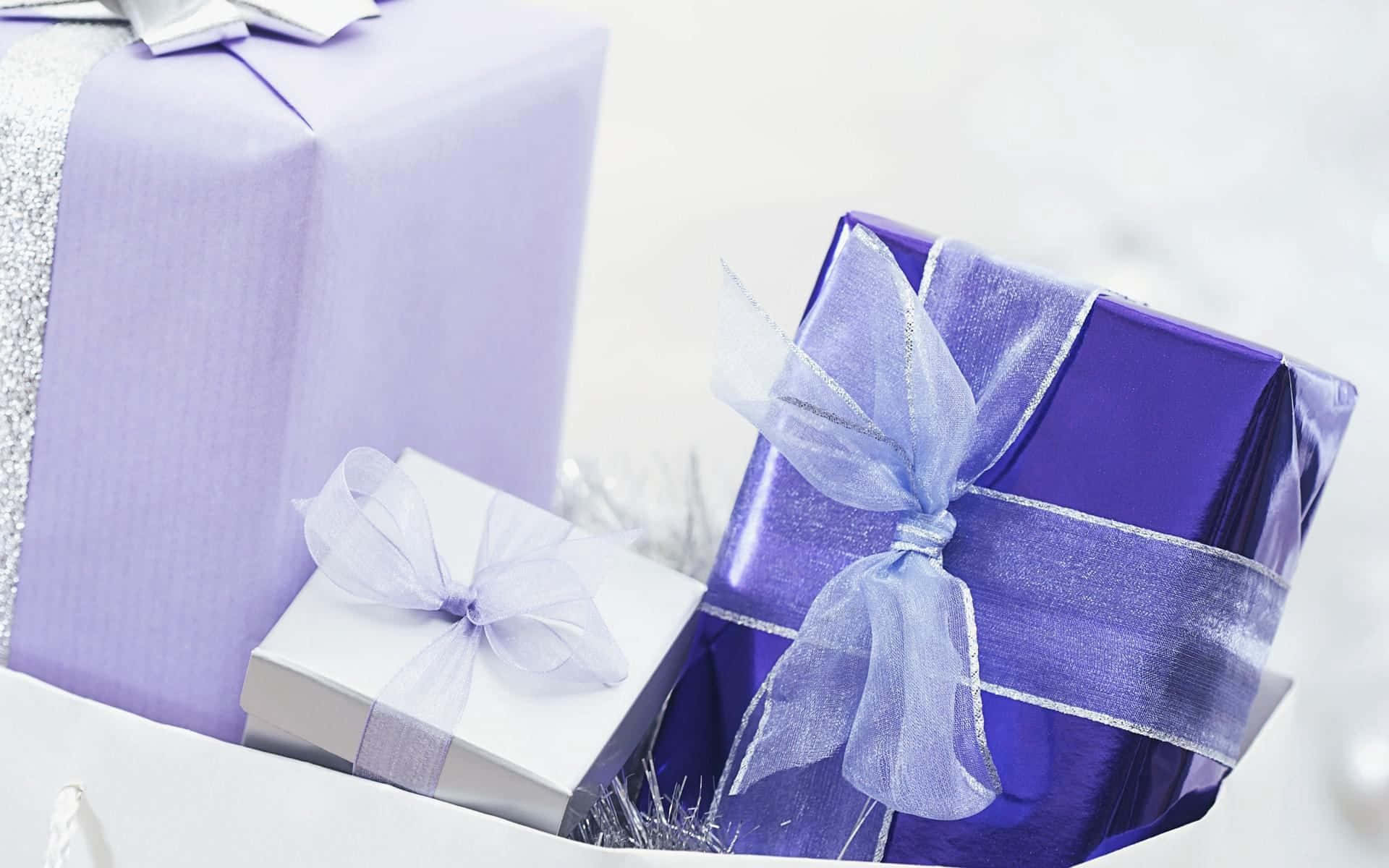 Gift 桌布 壁紙 — 三份優雅包裝的禮物，以薰衣草紫和白色為主，配上透明蝴蝶結，放在雪地上。