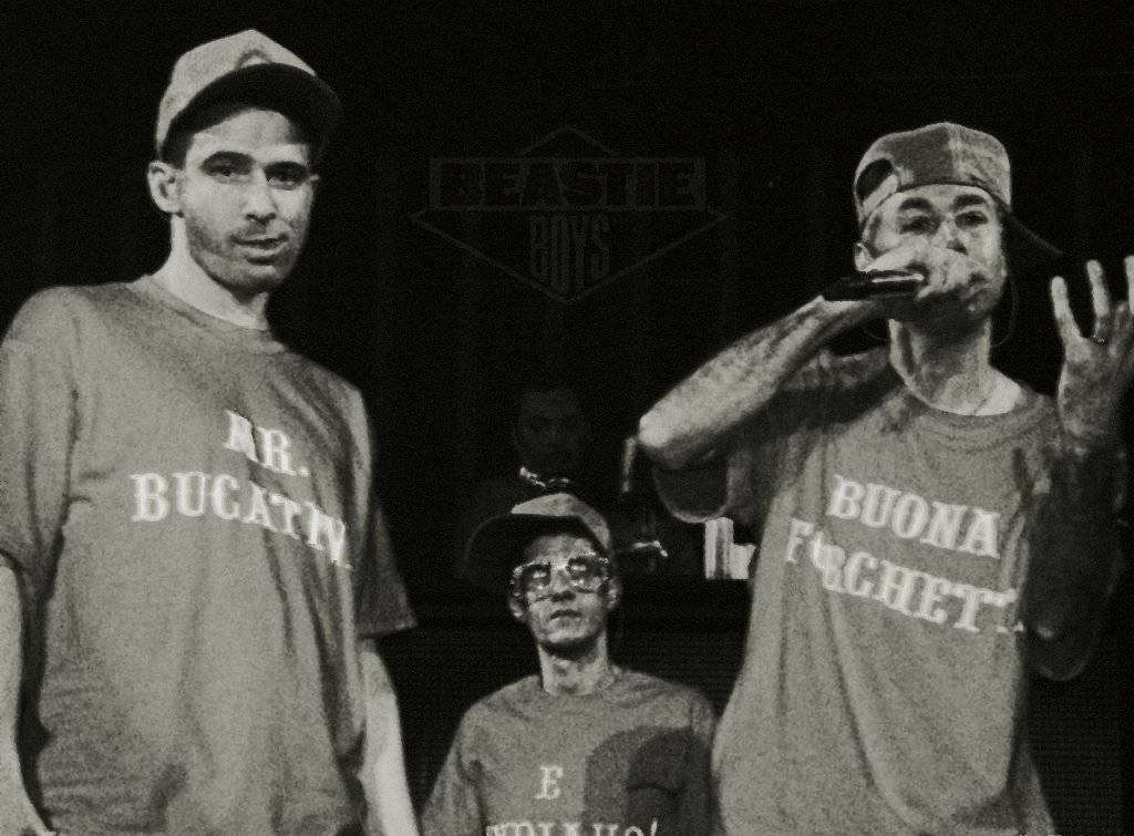 Rappers 桌布 壁紙 — 三位Beastie Boys成員以黑白風格在舞台上表演，身穿品牌T恤，其中一人對著麥克風說唱。