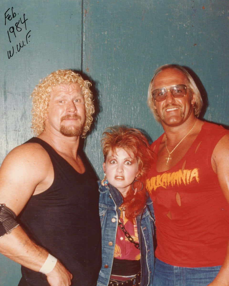 WWE 桌布 壁紙 — 三位WWE摔角手在1984年的復古照片中，在青綠色牆壁前擺出大膽表情和80年代時尚姿勢。