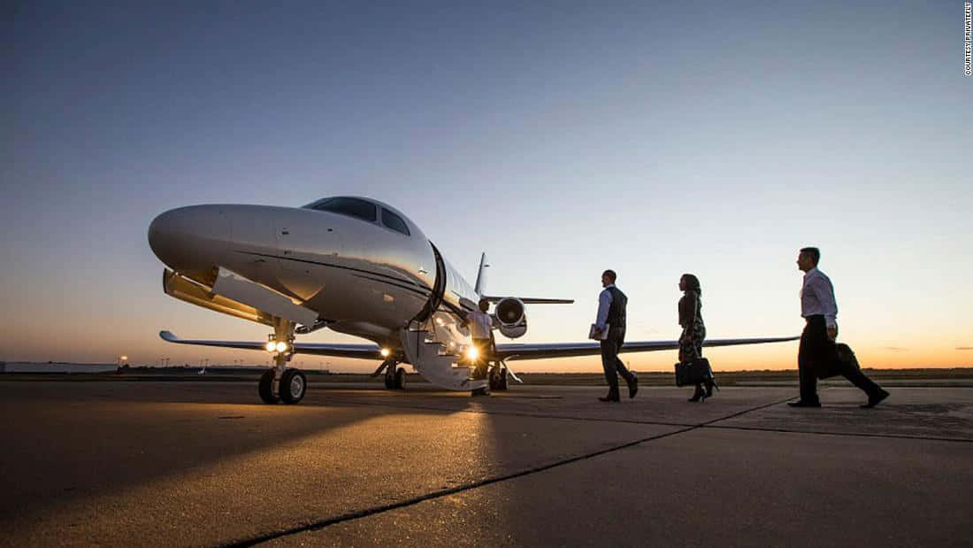 flying 桌布 壁紙 — 三位商務旅客在金色日落時分走向跑道上的私人飛機。