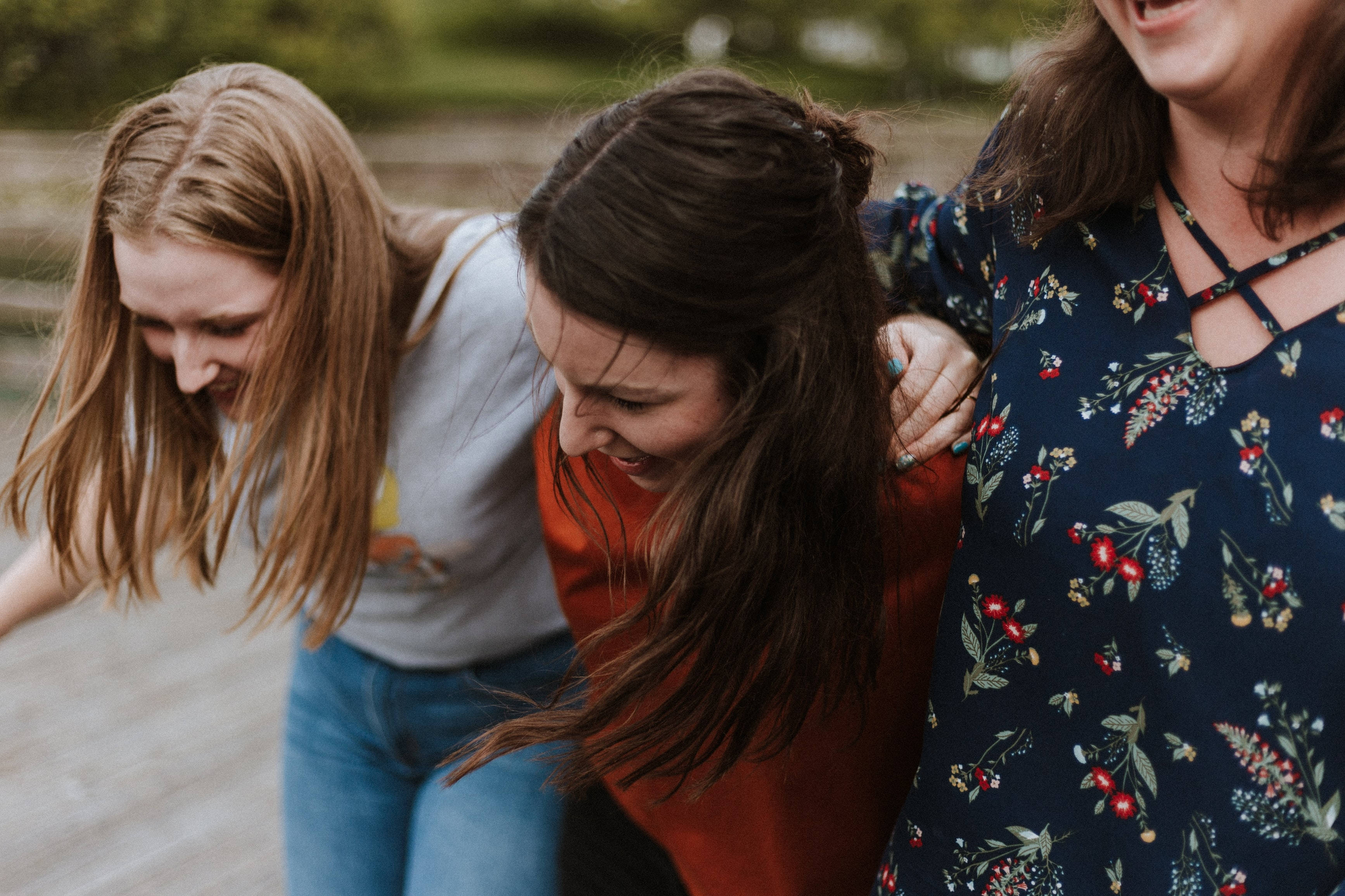 Teenage Girls 桌布 壁紙 — 三位大笑的女性在模糊的綠色背景中，一起享受歡樂的戶外時刻。