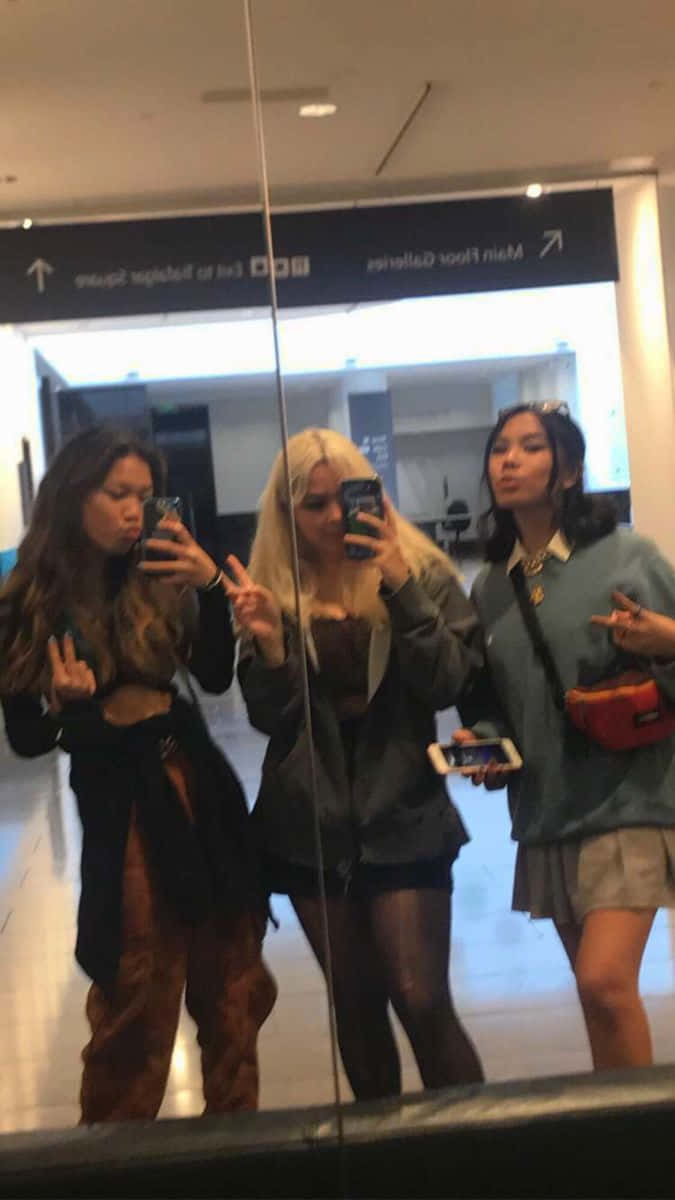 Friends 桌布 壁紙 — 三位年輕女性在商場鏡子前擺姿勢自拍，做出俏皮的手勢，穿著時尚的服裝。
