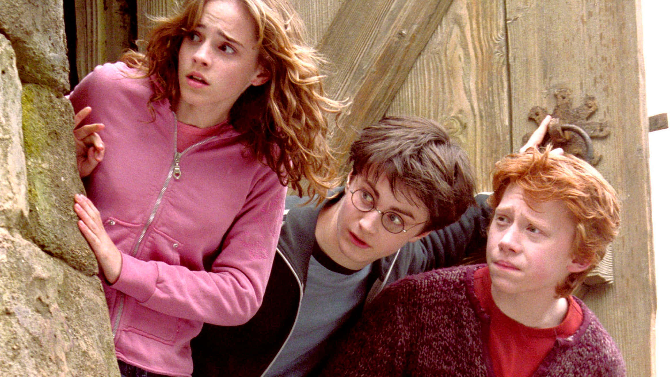 The Prisoner Of Azkaban 桌布 壁紙 — 三位年輕巫師睜大眼睛，小心翼翼地從石牆和木門旁窺視。