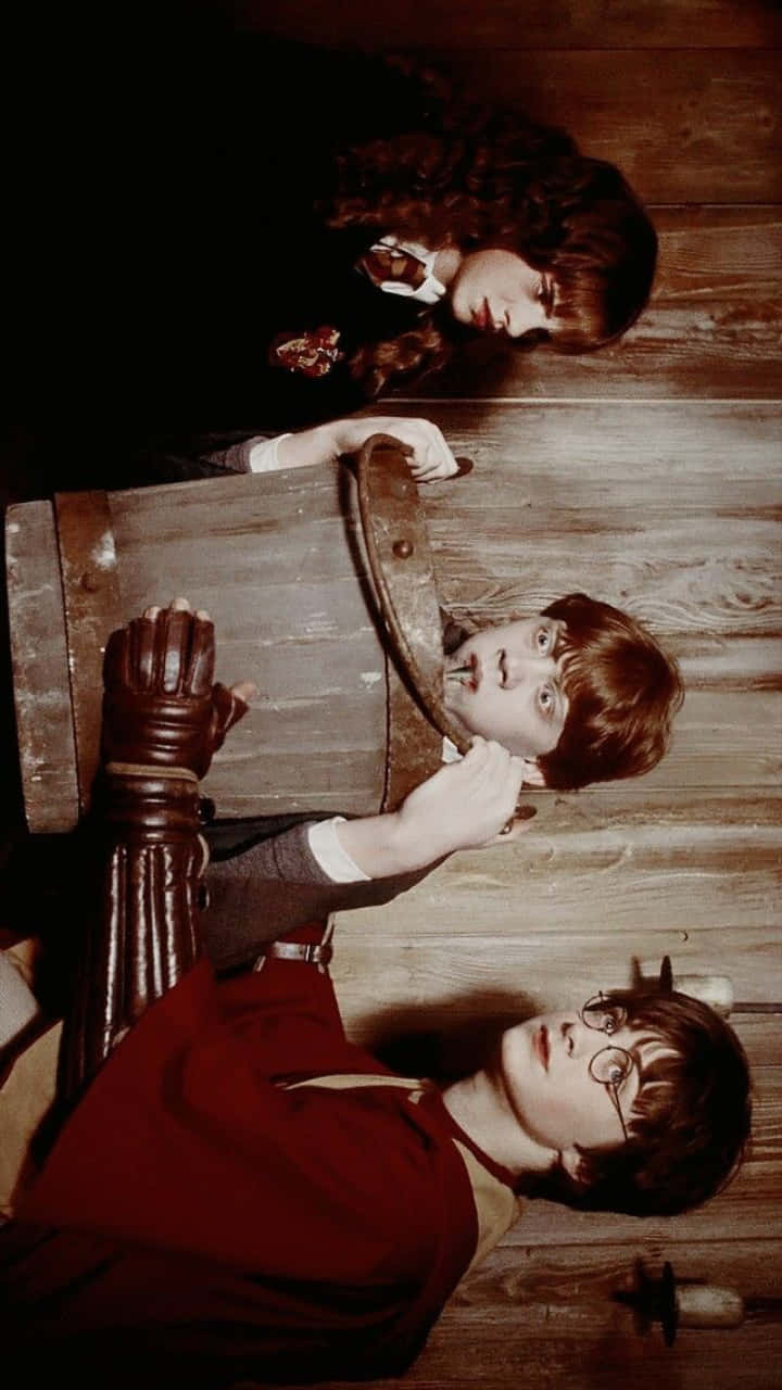 Ron Weasley 桌布 壁紙 — 三位年輕巫師躺在昏暗房間的木地板上，一人透過木桶窺視，另外兩人抬頭露出驚訝和好奇的表情。