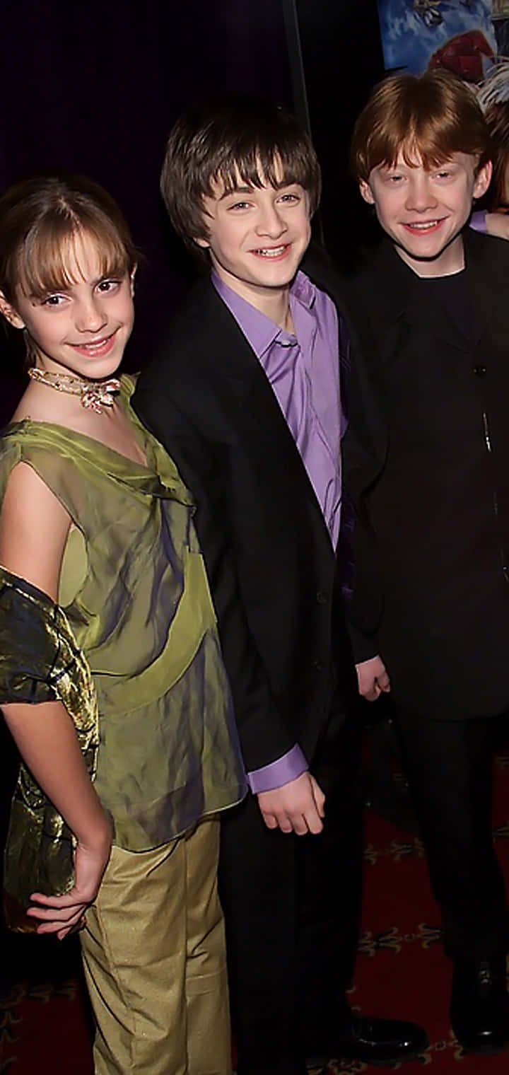Golden Trio 桌布 壁紙 — 三位年輕演員穿著正式服裝，在明亮的活動燈光下於紅地毯上微笑拍照。