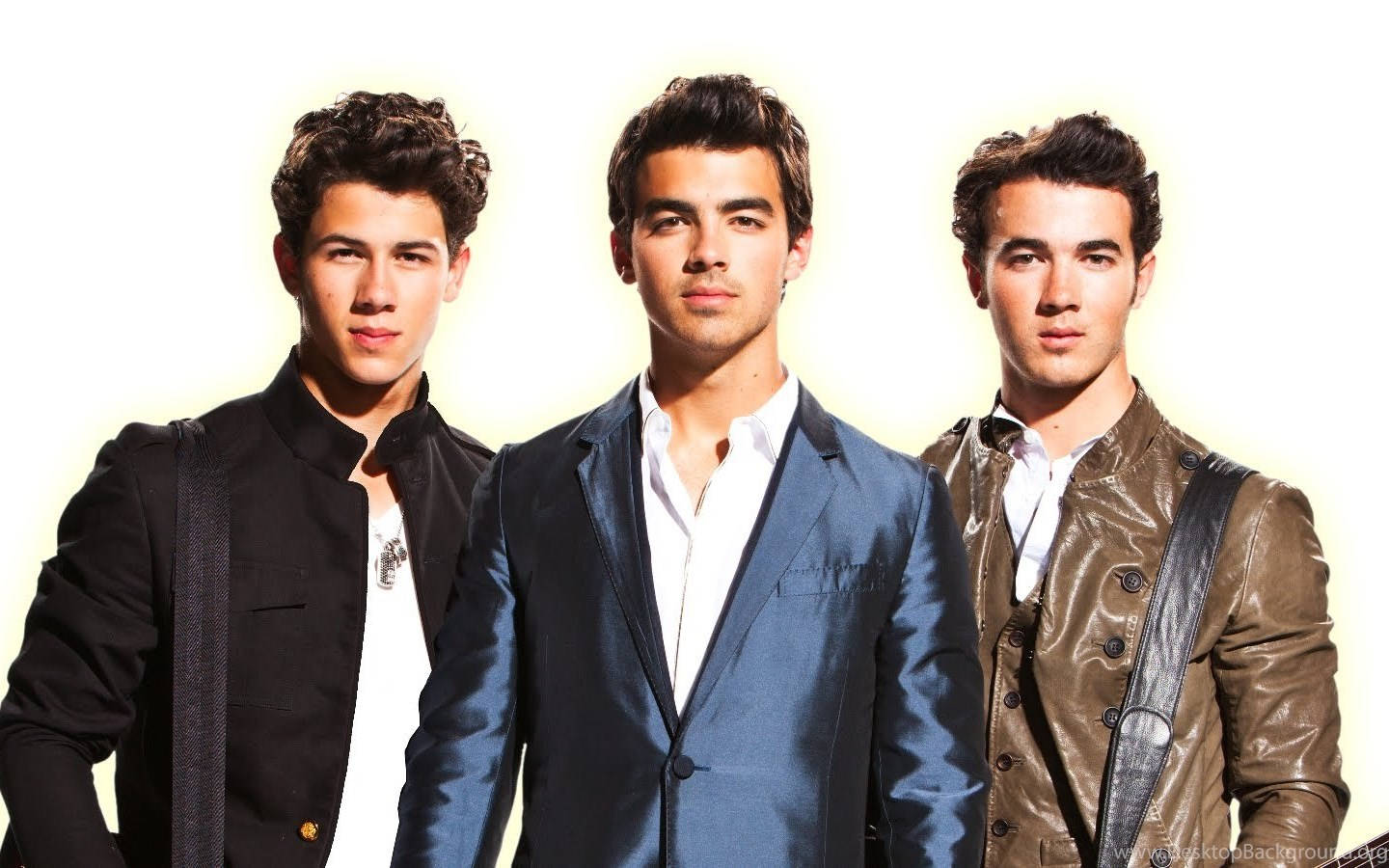 Jonas Brothers 桌布 壁紙 — 三位年輕男士身穿時尚外套，在明亮的白色背景前自信擺姿勢，配以柔和的金色燈光。